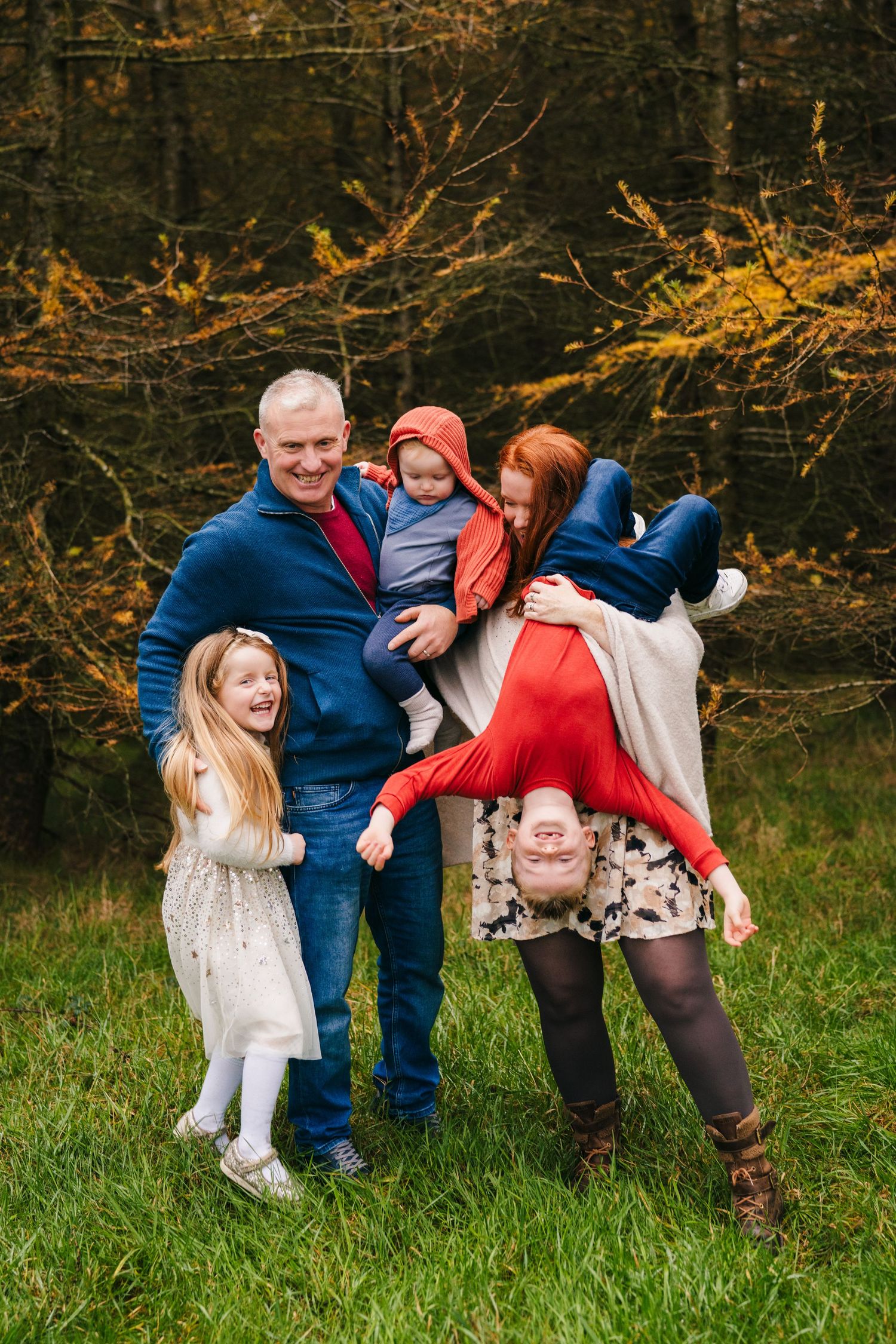 Playful family photoshoot on grass with everyone laughing and having fun.