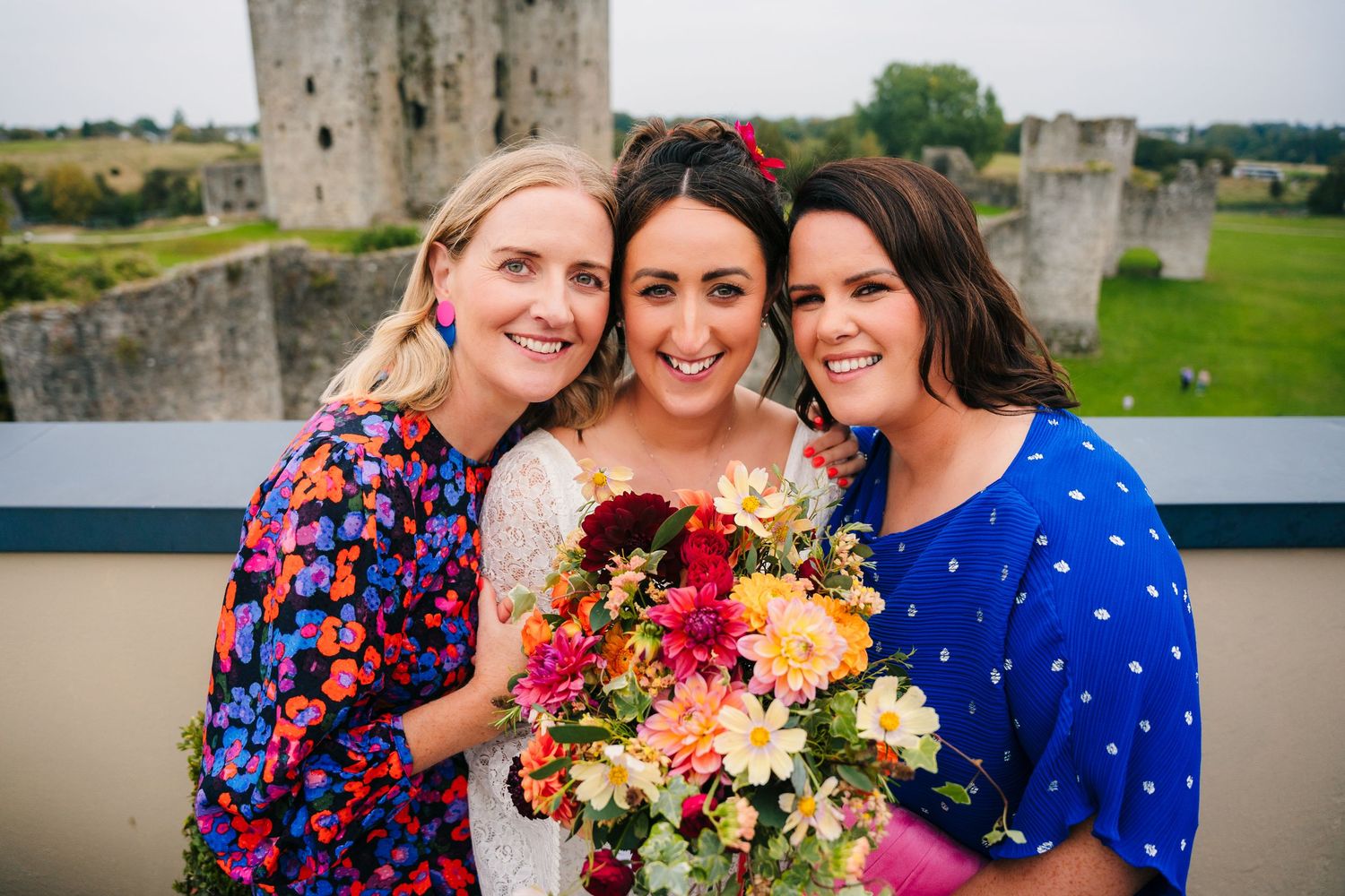 Cheerful wedding party poses with colorful bouquet against castle backdrop.Wedding Photography Trim Castle Ireland