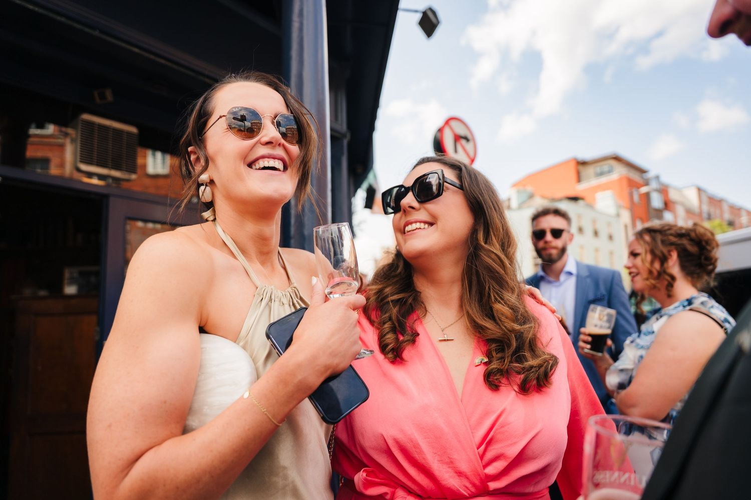People enjoying a sunny outdoor wedding gathering with brick buildings and blue sky in background. Same sex wedding PHOTOGRAPHER Dublin