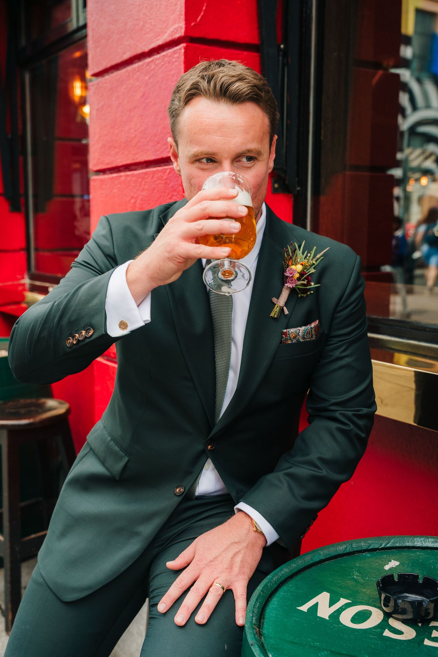 Wedding party enjoying drinks at an outdoor venue with red wall background. Same sex wedding PHOTOGRAPHER Dublin