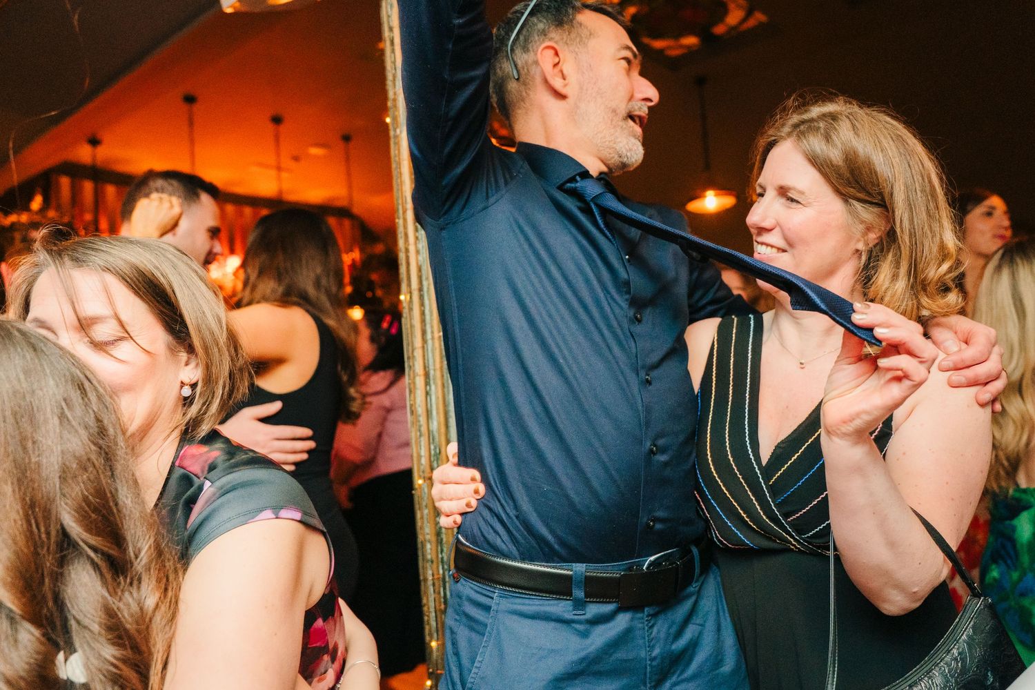 Party guests dancing and singing together in a dimly lit venue with warm orange lighting. Marco Pierre Dublin Wedding Photographer