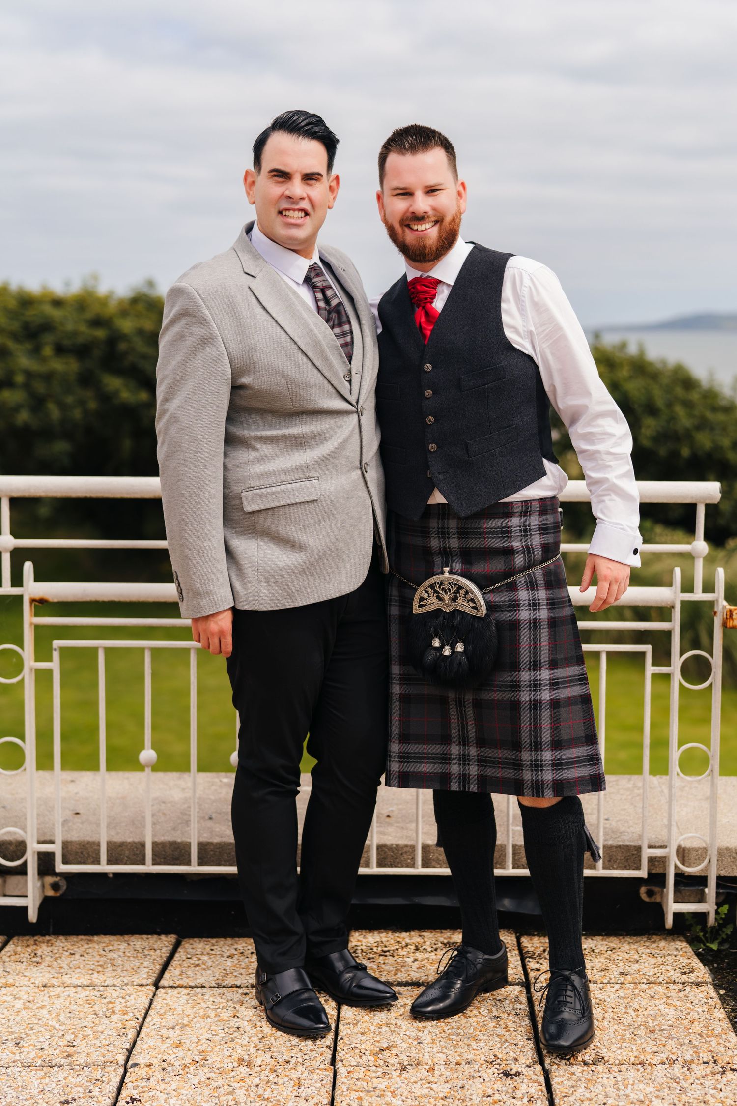 Men wearing traditional Scottish kilts and formal attire posing together on outdoor patio during wedding celebration. Portmarnock Hotel Wedd