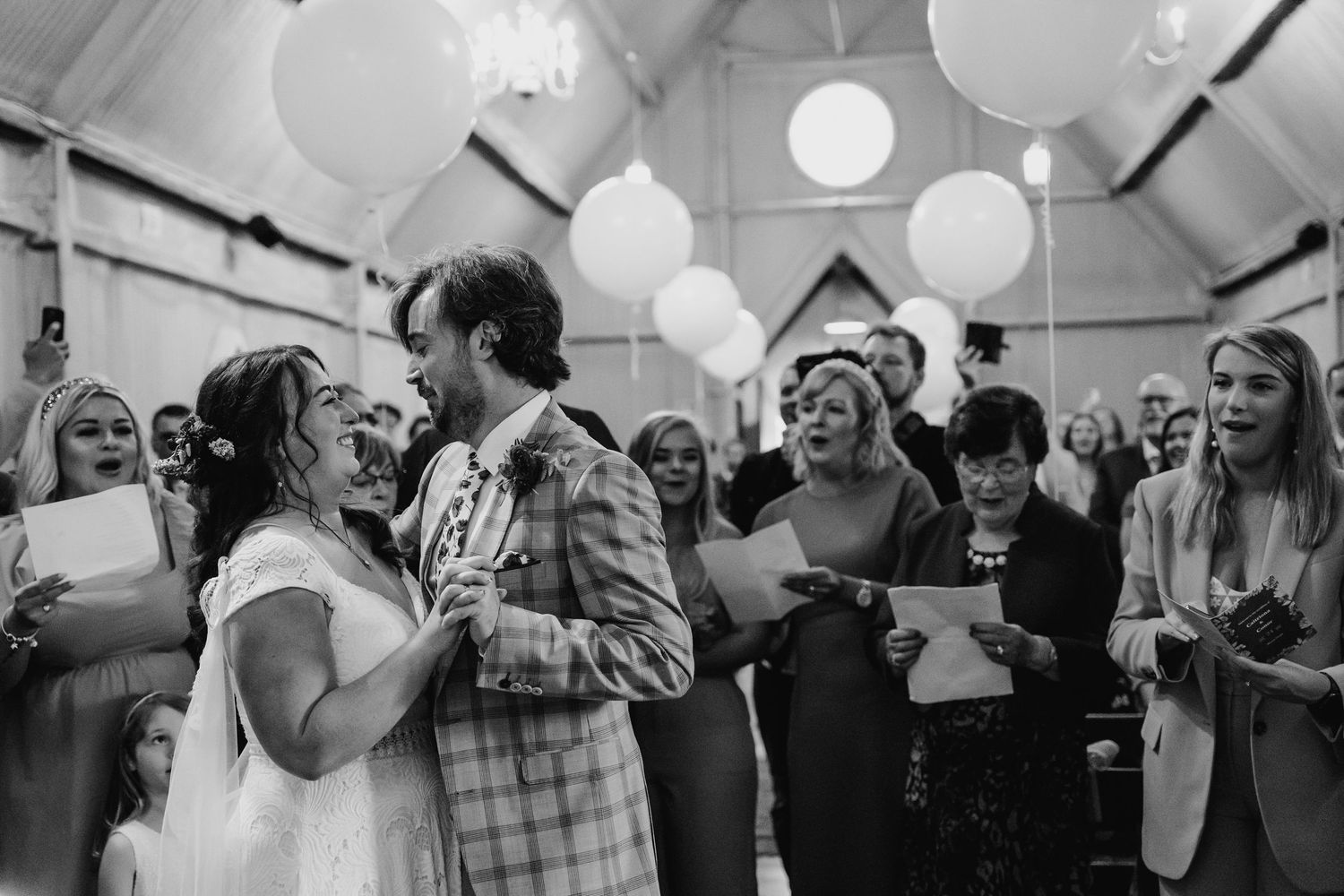 Wedding reception guests enjoying themselves under paper lanterns in a vaulted ceiling venue. Wedding photographer Dublin