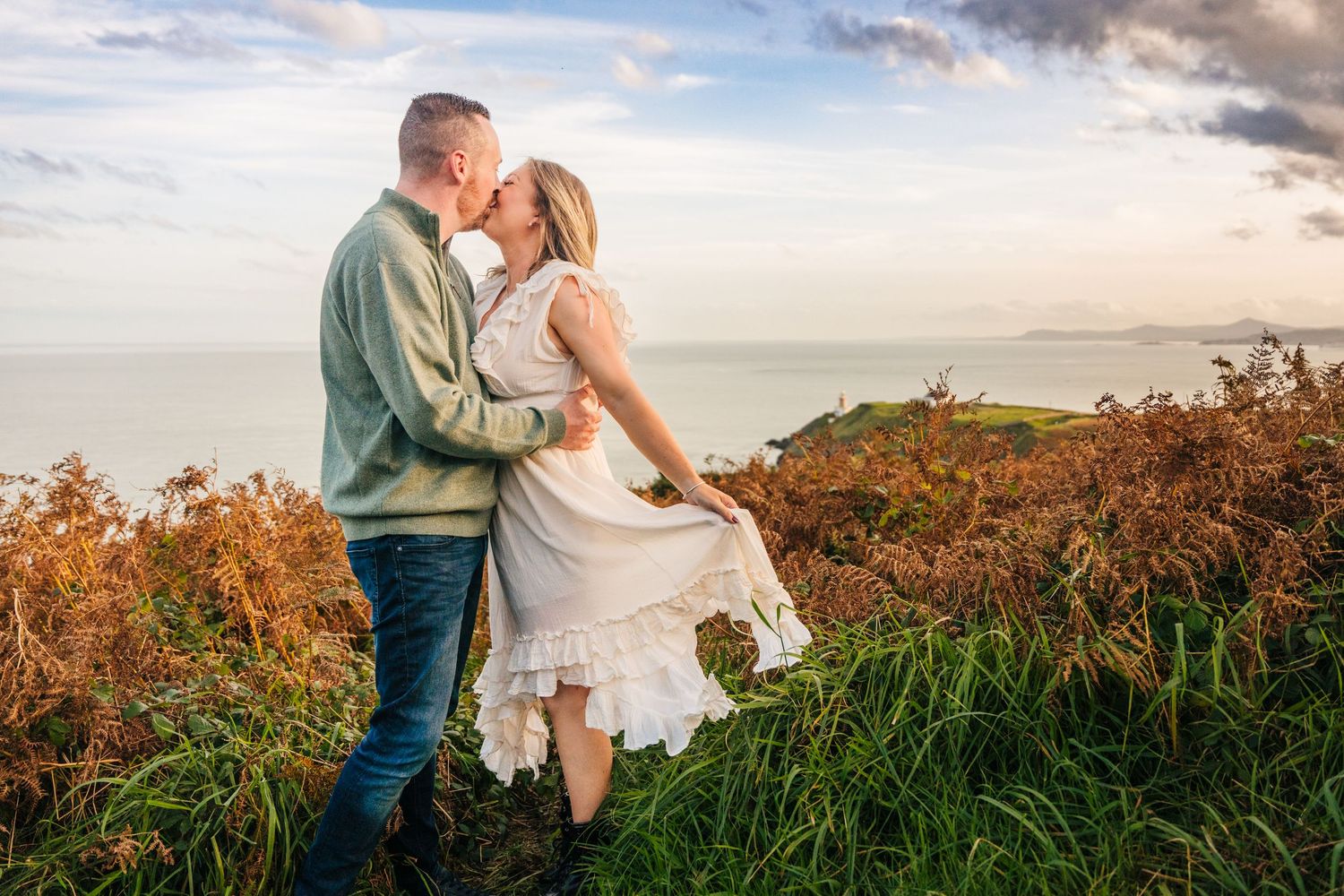 A couple embraces against a golden sunset backdrop on a hilltop surrounded by tall autumn grasses and wildflowers. PHOTOGRAPHER Dublin irela