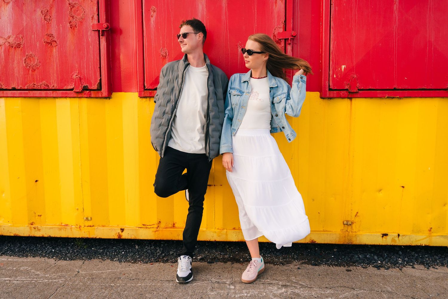 Stylish couple in denim jackets poses against vibrant red and yellow shipping container wall. PHOTOGRAPHER Dublin ireland