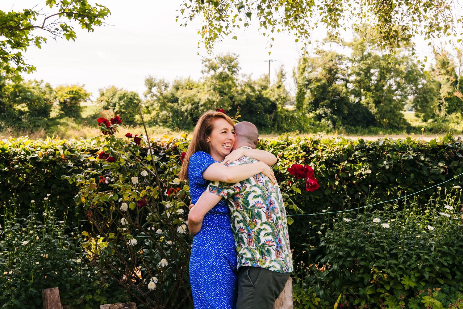 Two people embrace in a garden setting with blooming roses and greenery during golden hour. PHOTOGRAPHER Dublin ireland