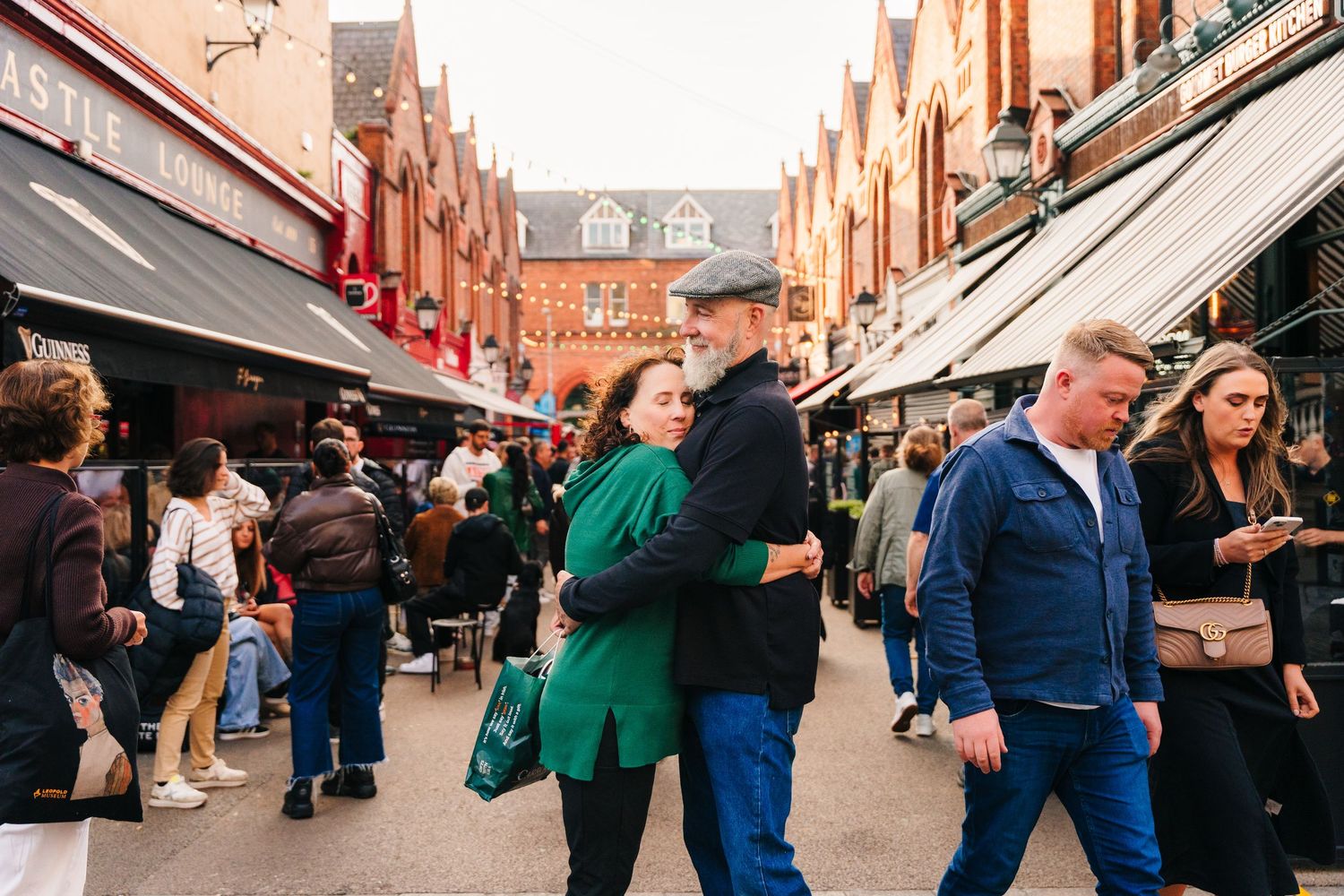 Bustling scene at a market street with shoppers and vendors under a row of brick buildings with awnings. PHOTOGRAPHER Dublin