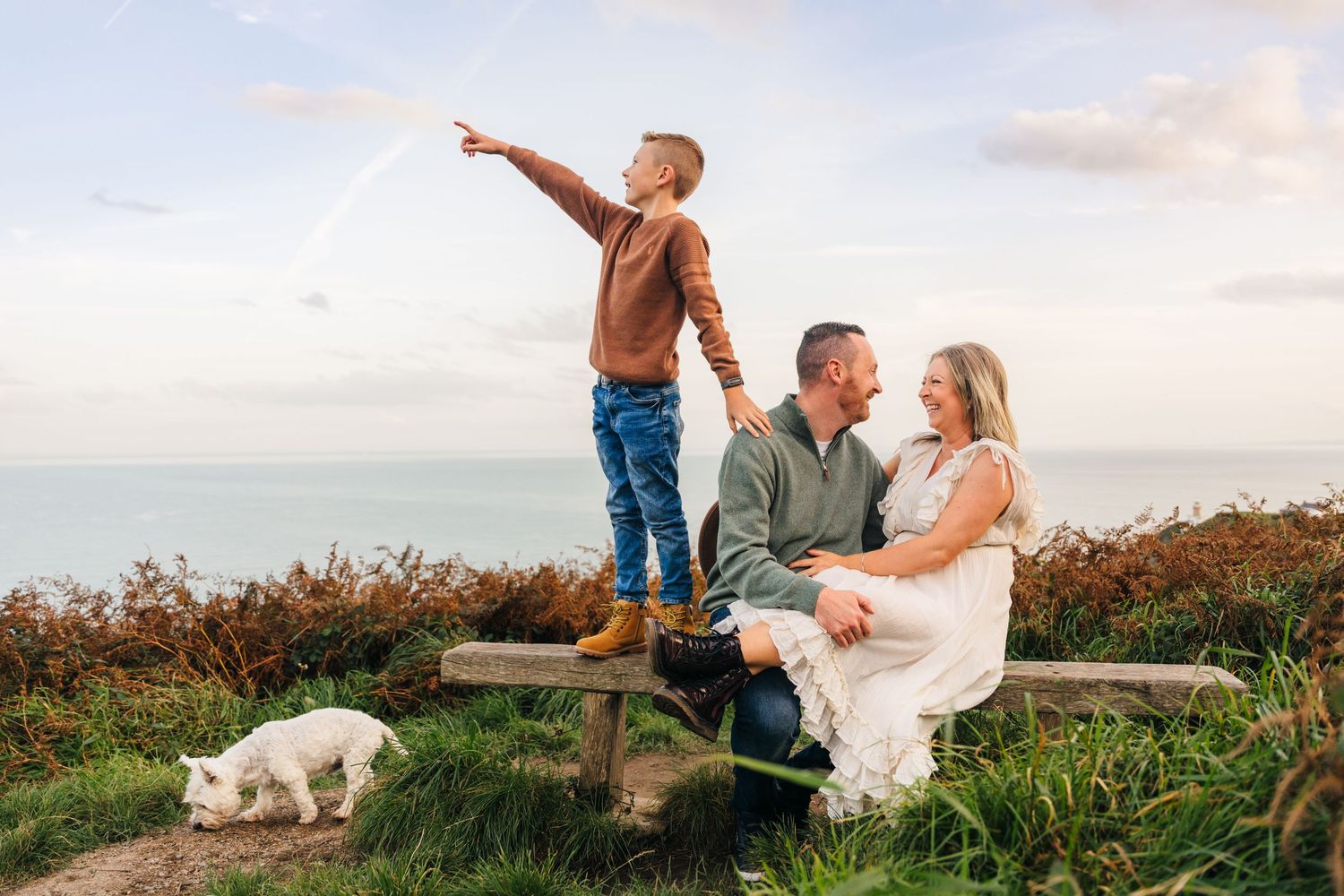 Couple shares romantic moments at sunset in an outdoor meadow field with their small white dog nearby. Family PHOTOGRAPHER Dublin