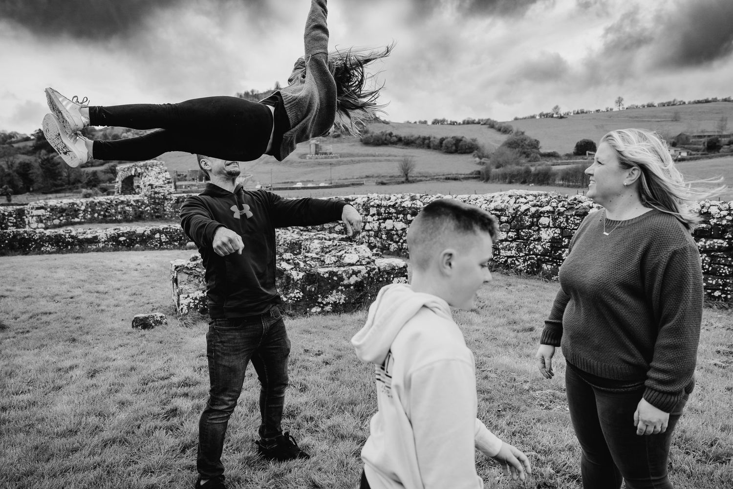 People having fun in a field with one person leaping horizontally in the air in black and white tones. family PHOTOGRAPHER Dublin