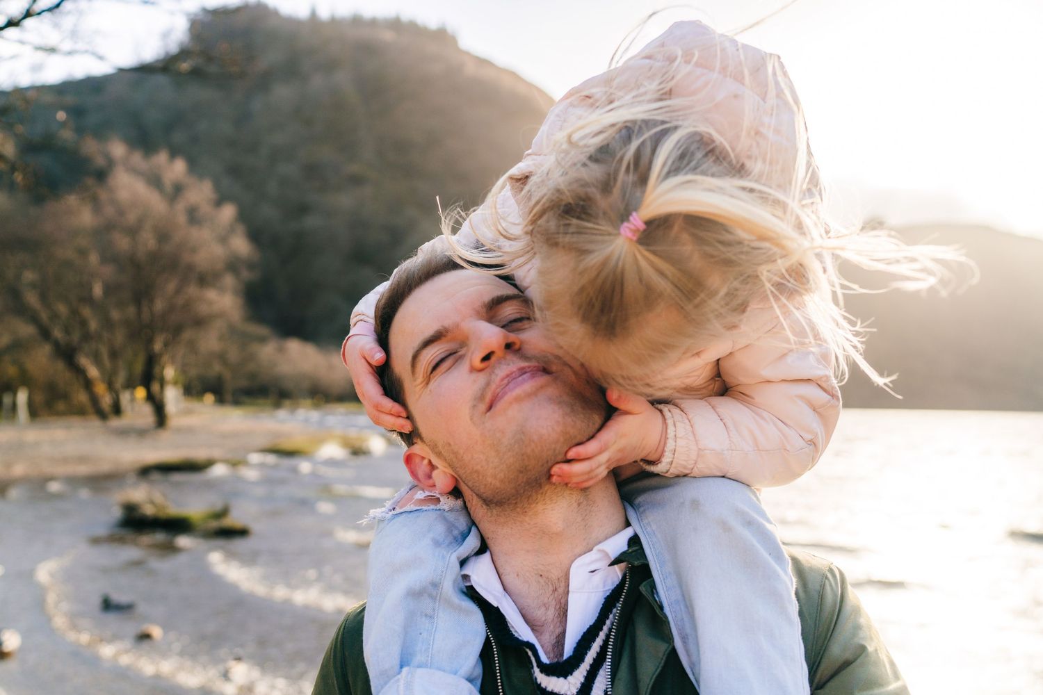 A romantic couple kisses at the lakeside during golden hour sunset with mountains in the background. family PHOTOGRAPHER Dublin