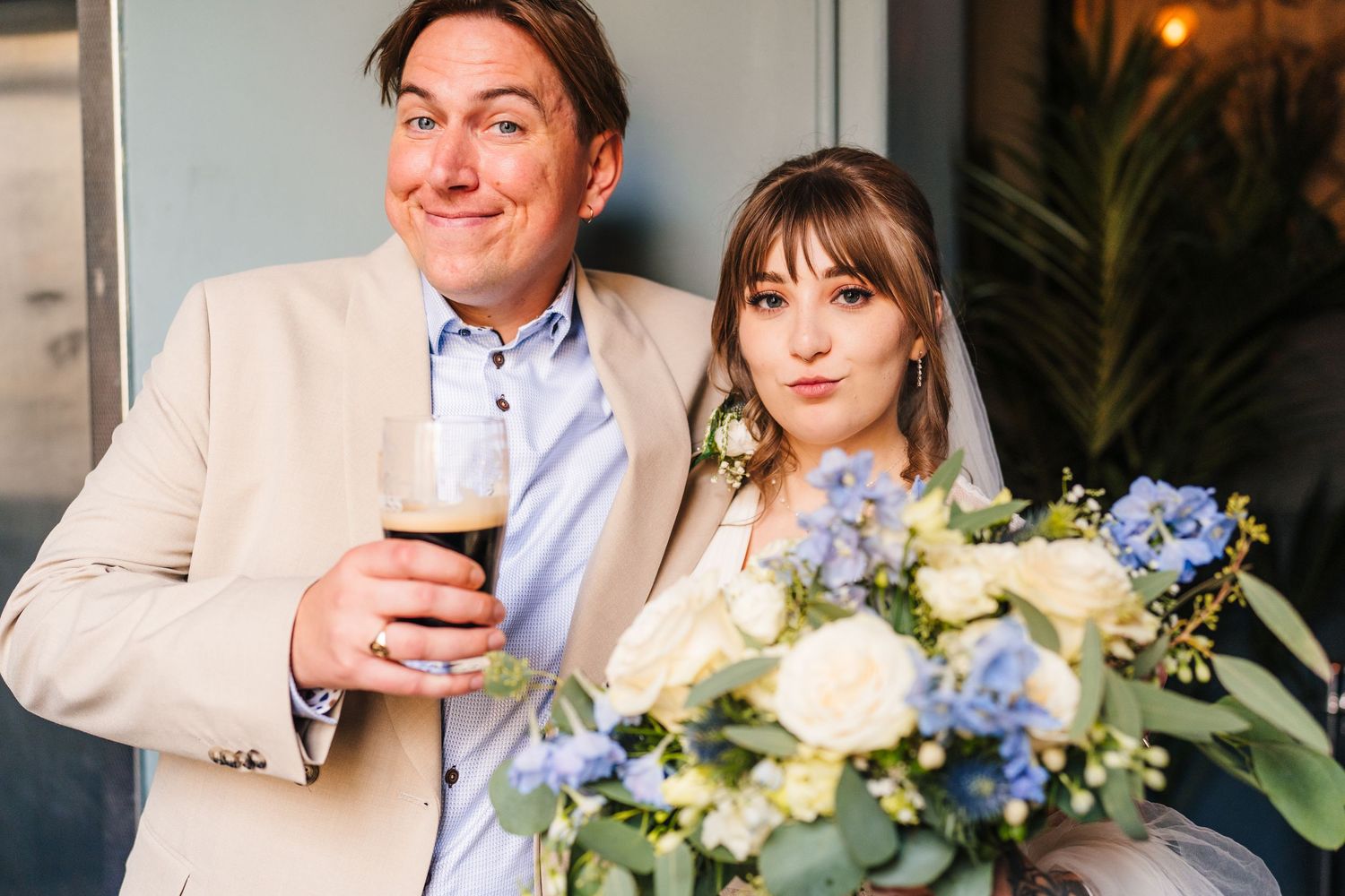 Two happy wedding guests smile while holding a glass of wine with a blue and white floral bouquet in view. Wedding PHOTOGRAPHER Dublin