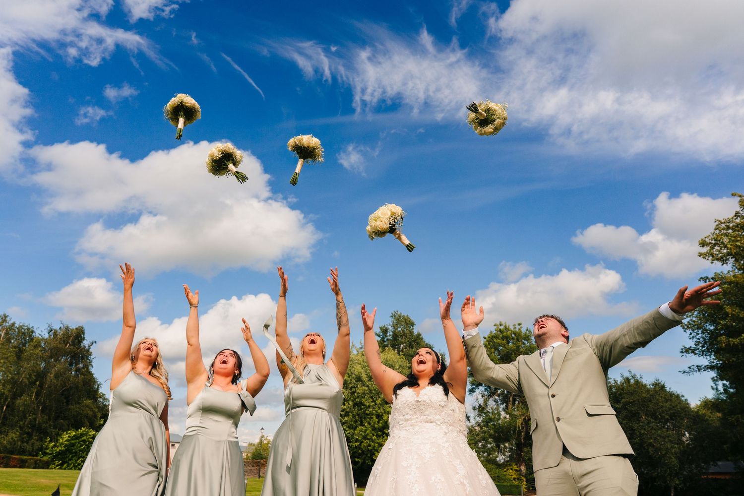 A wedding party throws yellow bouquets into the blue sky during an outdoor celebration. Wedding PHOTOGRAPHER Dublin