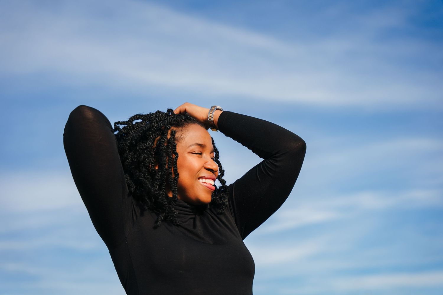 Person in black top and beige coat poses against vibrant blue sky. Dublin professional headshots photographer
