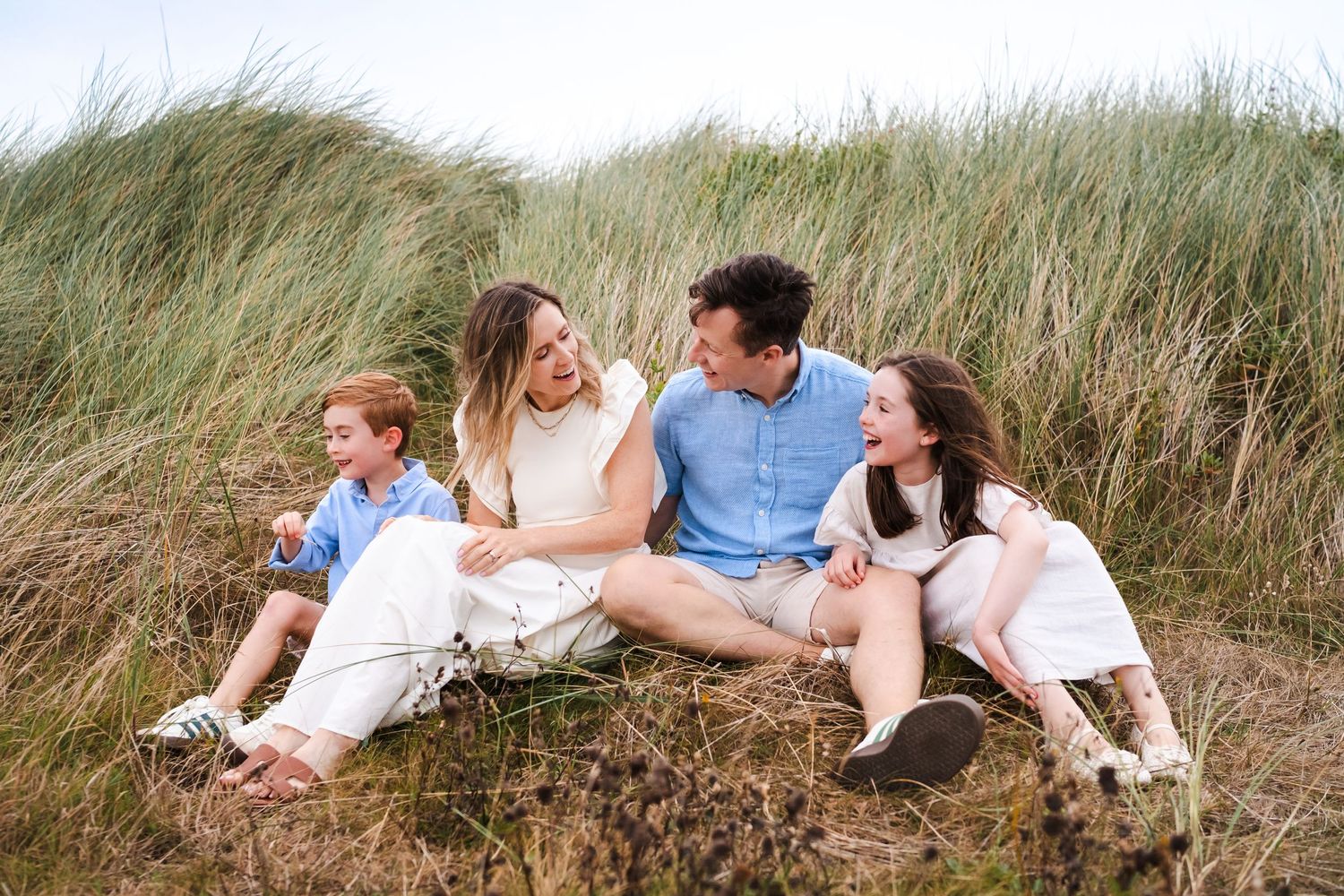 A group of people relax together in tall grass during a warm summer day near the beach.  Family photographer Dublin Ireland