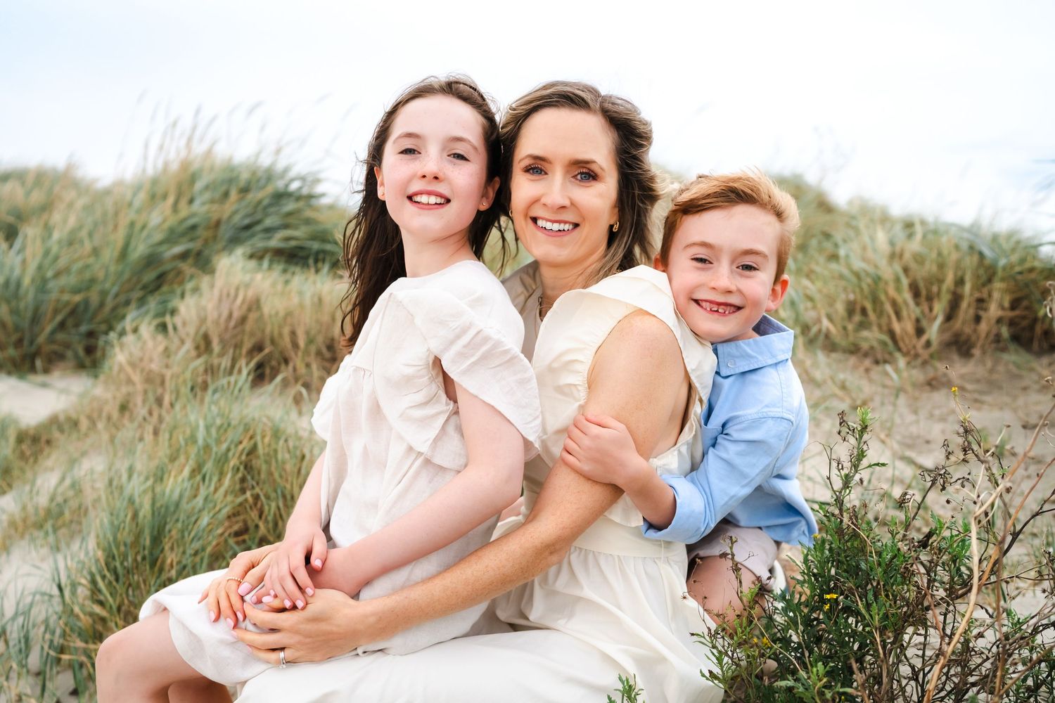People embracing and sharing joyful moments among coastal dunes on a sunny afternoon.  Family photographer Dublin Ireland