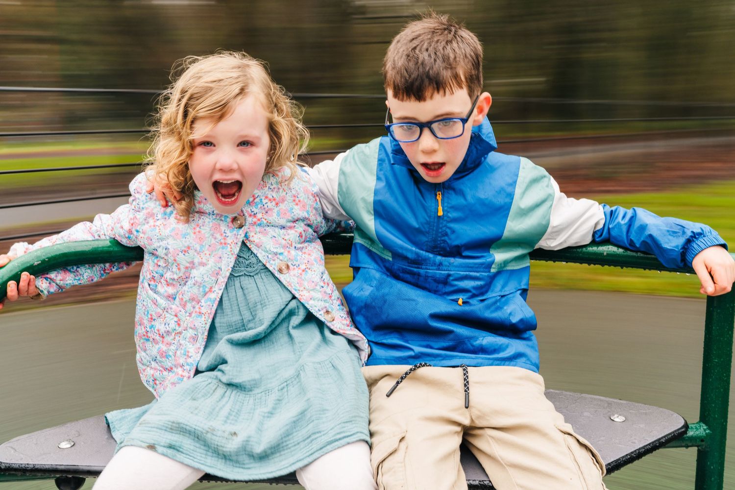 Family photographer Dublin Ireland  Two children laugh and play together while riding on playground equipment.