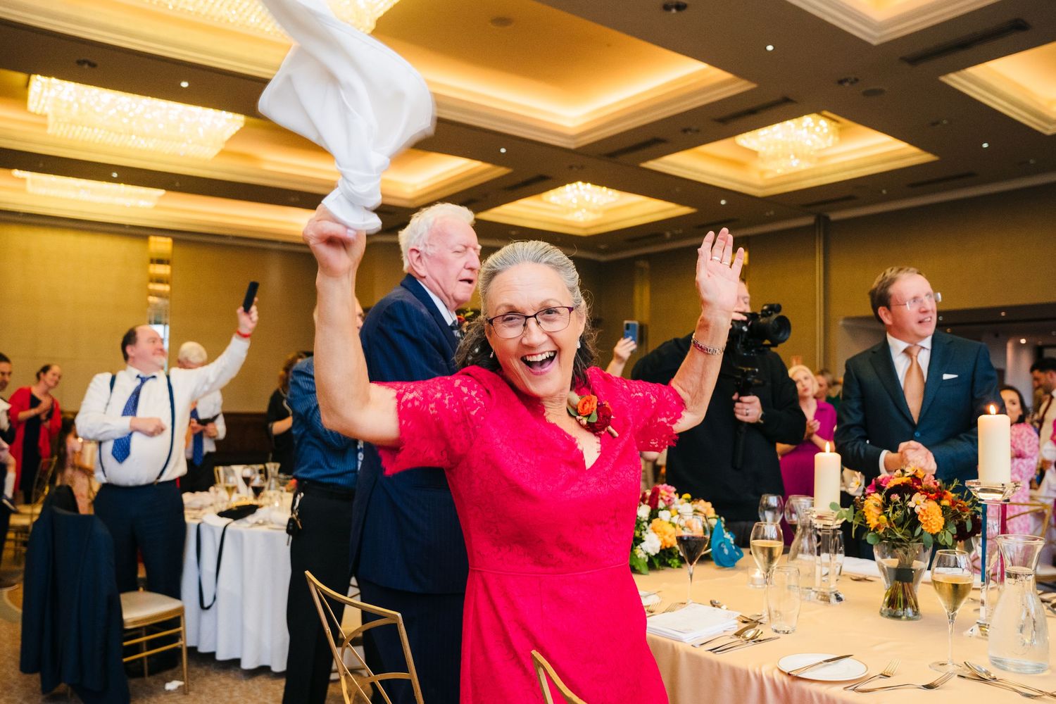 Wedding guests celebrate joyfully at a reception with elegant ceiling lighting and floral centerpieces.Wedding Photography Trim Castle Irela