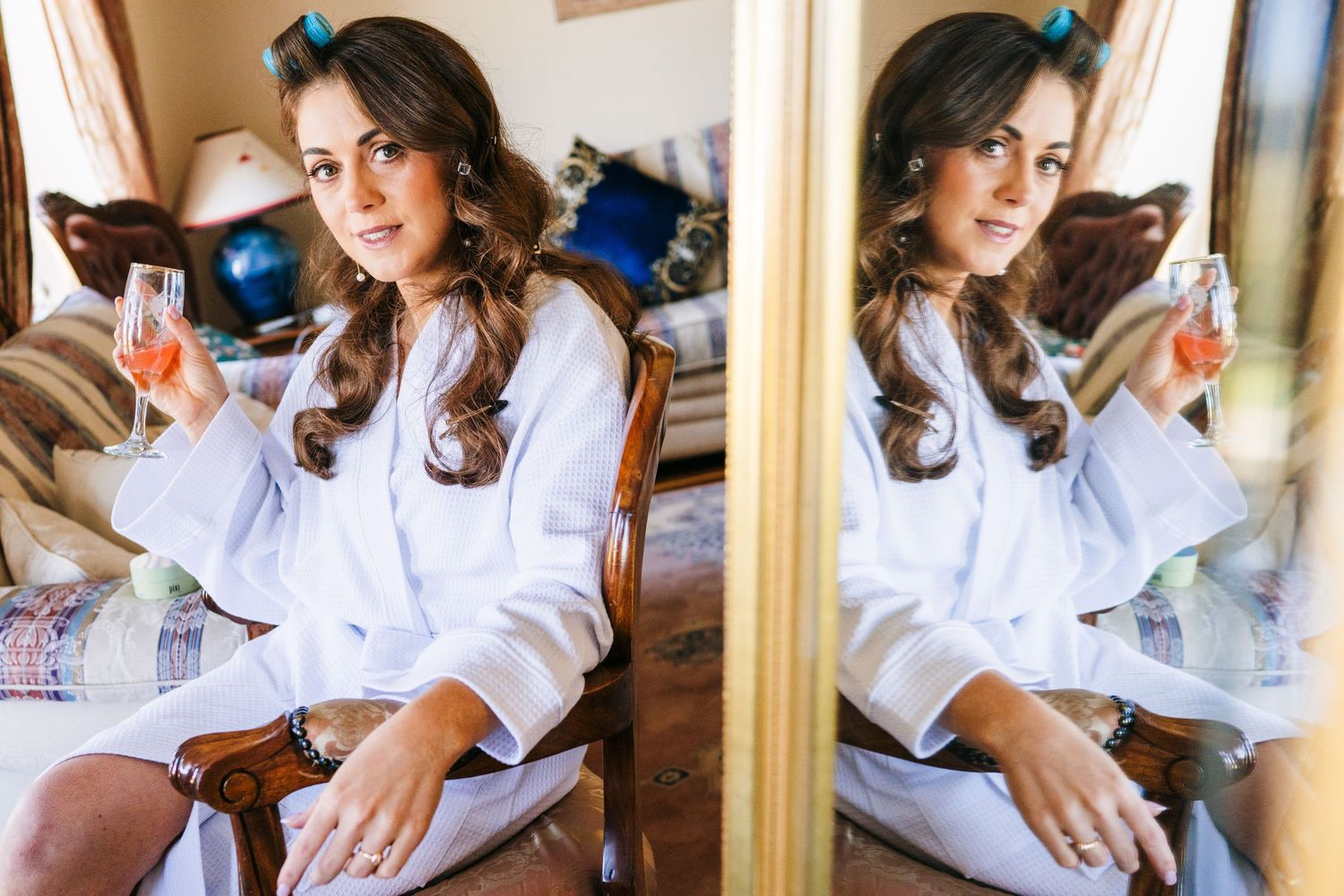 Person in white robe sitting at vanity mirror holding cosmetic bottles in morning light. Castle Leslie Wedding Photographer Dublin