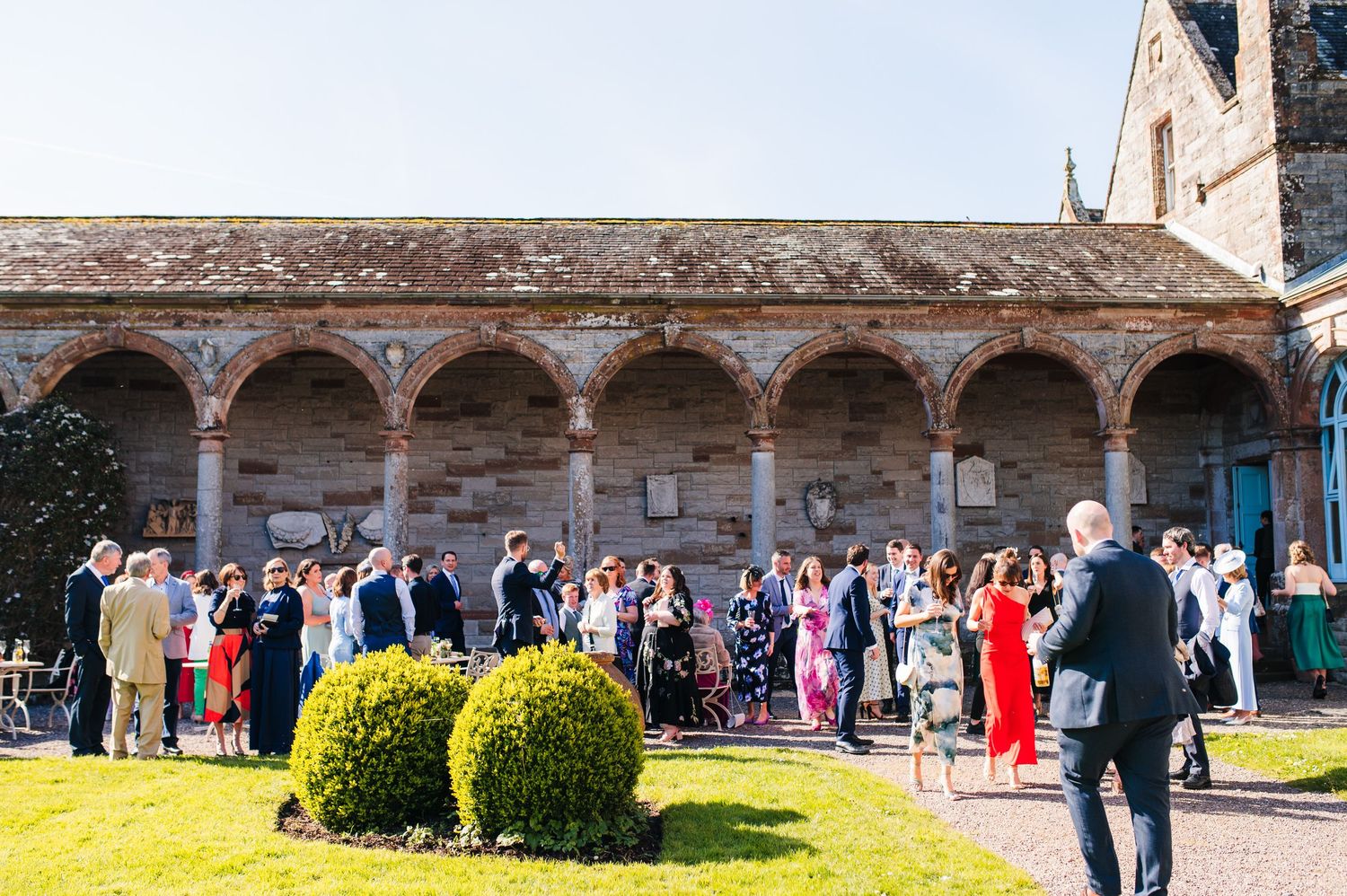 Castle Leslie Wedding Photographer Dublin Wedding guests gathered in courtyard with beautiful stone archway and manicured gardens.