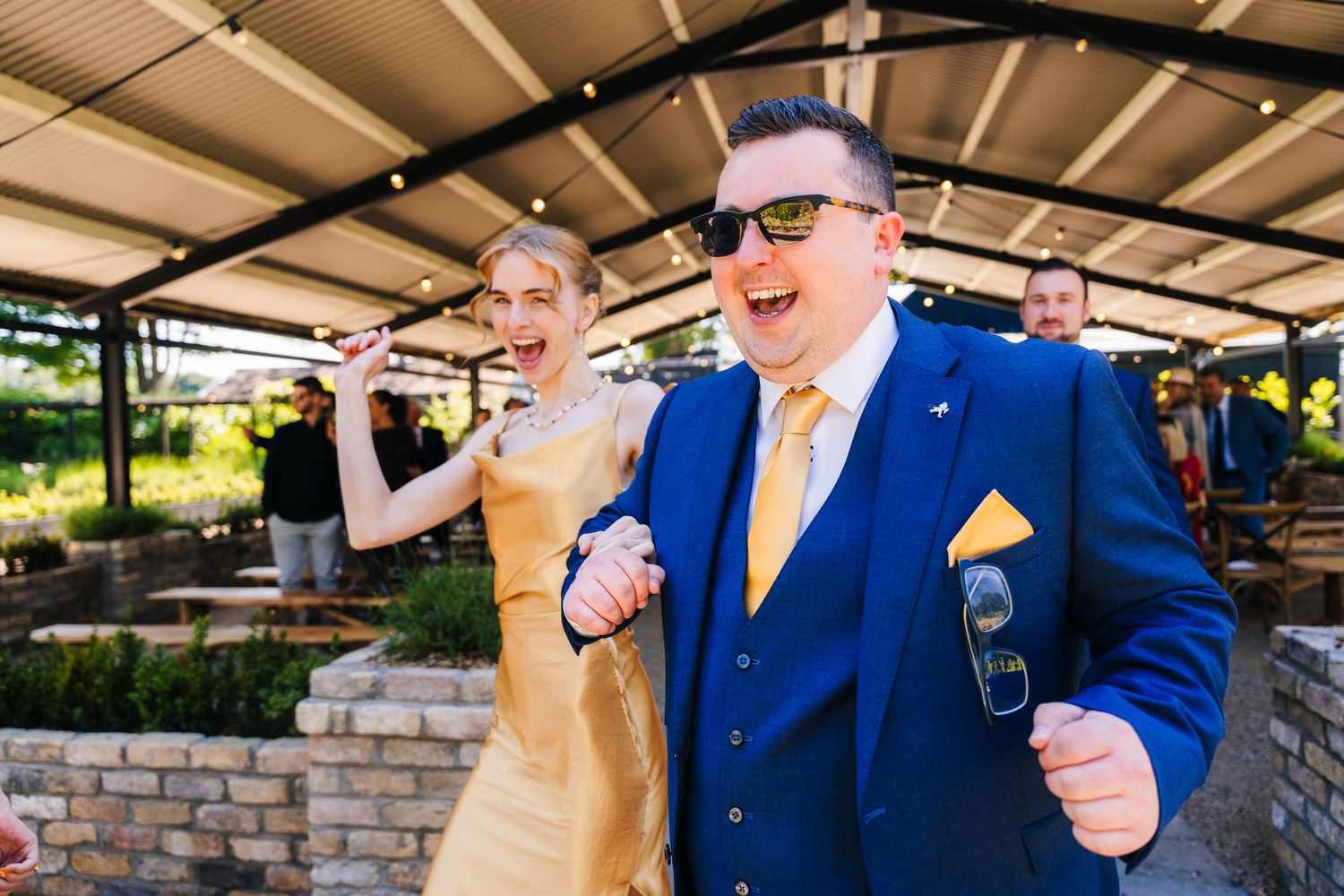 Wedding guests dancing and celebrating with drinks at an outdoor reception.