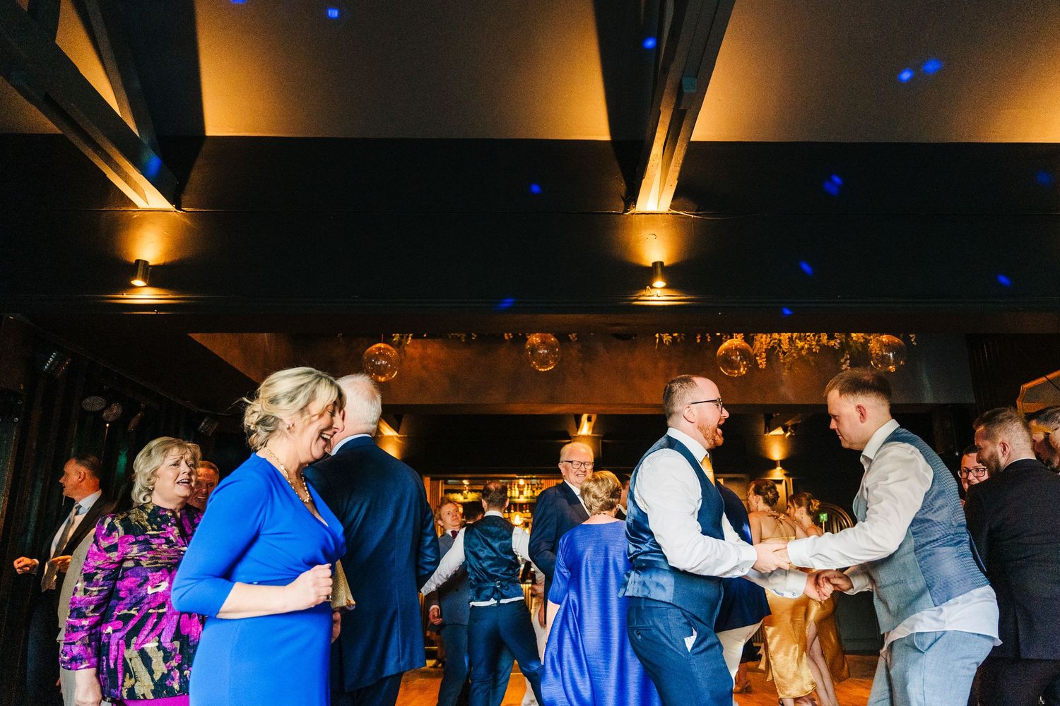 Poulaphouca Wedding photographer wicklow Wedding guests dancing and celebrating in a warmly lit reception venue with exposed wooden beams.