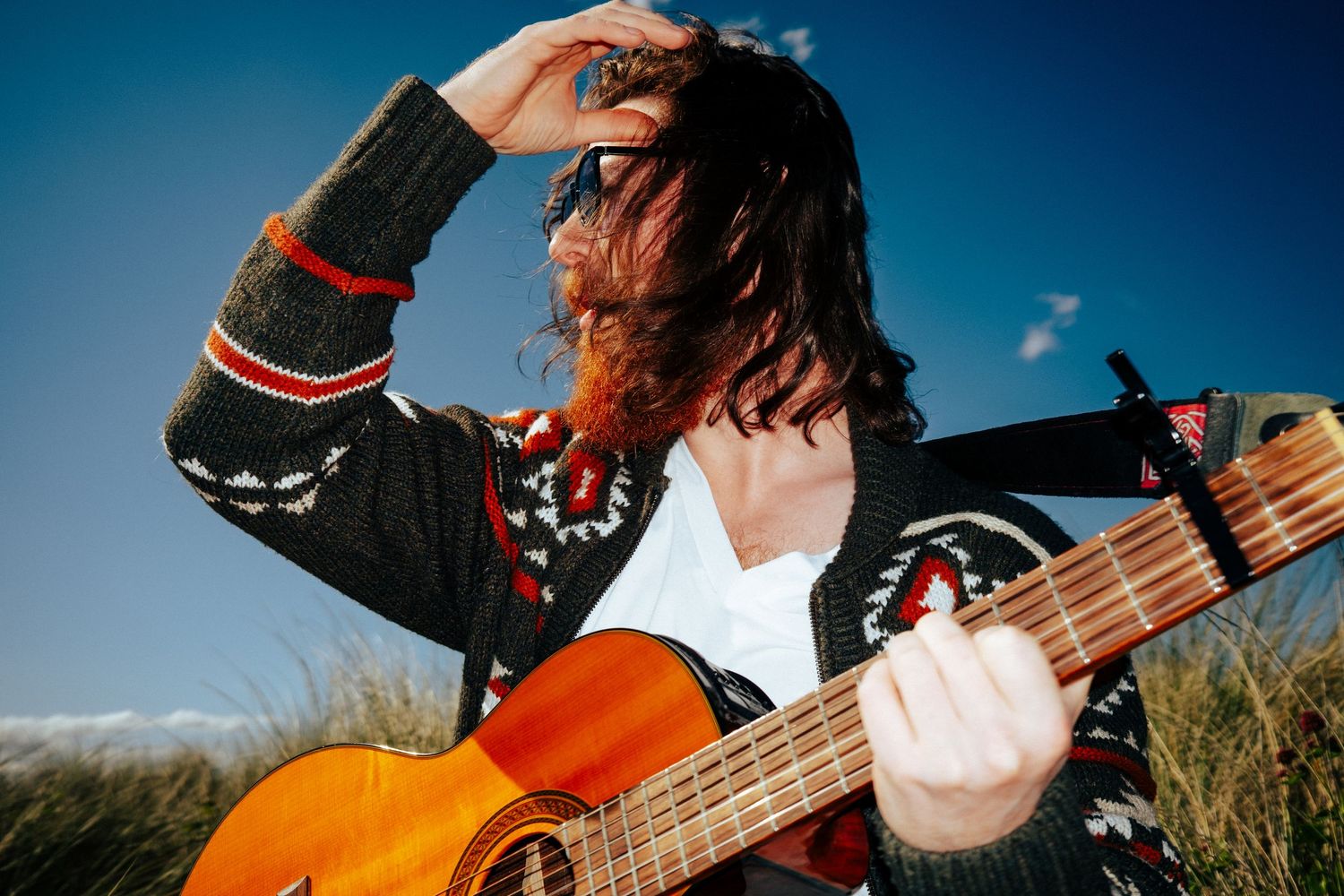Musician plays acoustic guitar outdoors with dramatic blue sky background. PHOTOGRAPHER Dublin