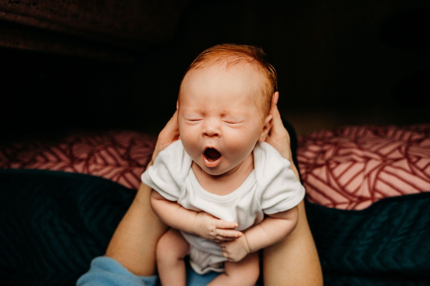 A baby in a white outfit sits on red patterned fabric showing various expressions and poses. Family PHOTOGRAPHER Dublin