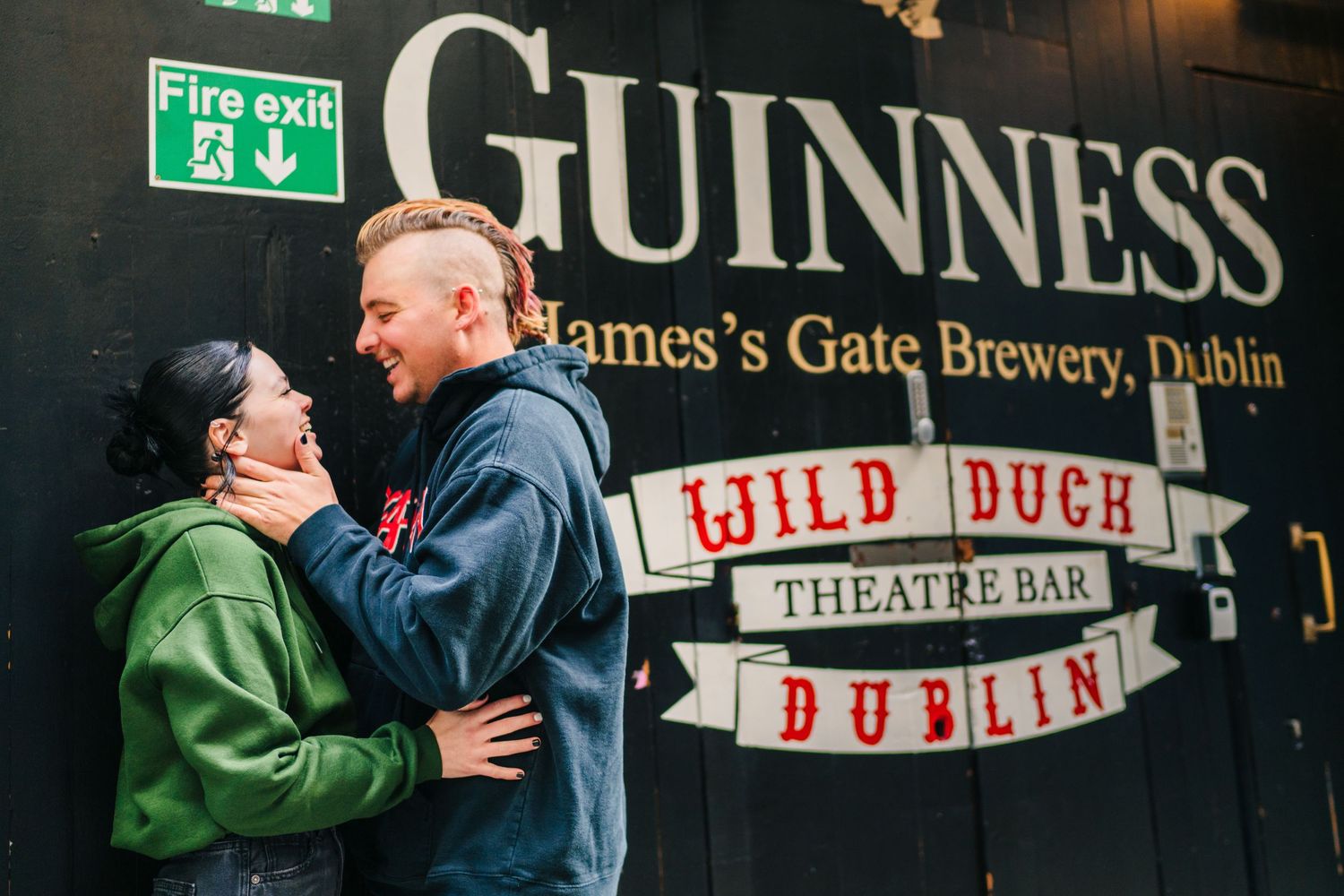 A couple embraces near the Guinness brewery and Wild Duck Theatre Bar signs in Dublin. PHOTOGRAPHER Dublin Ireland