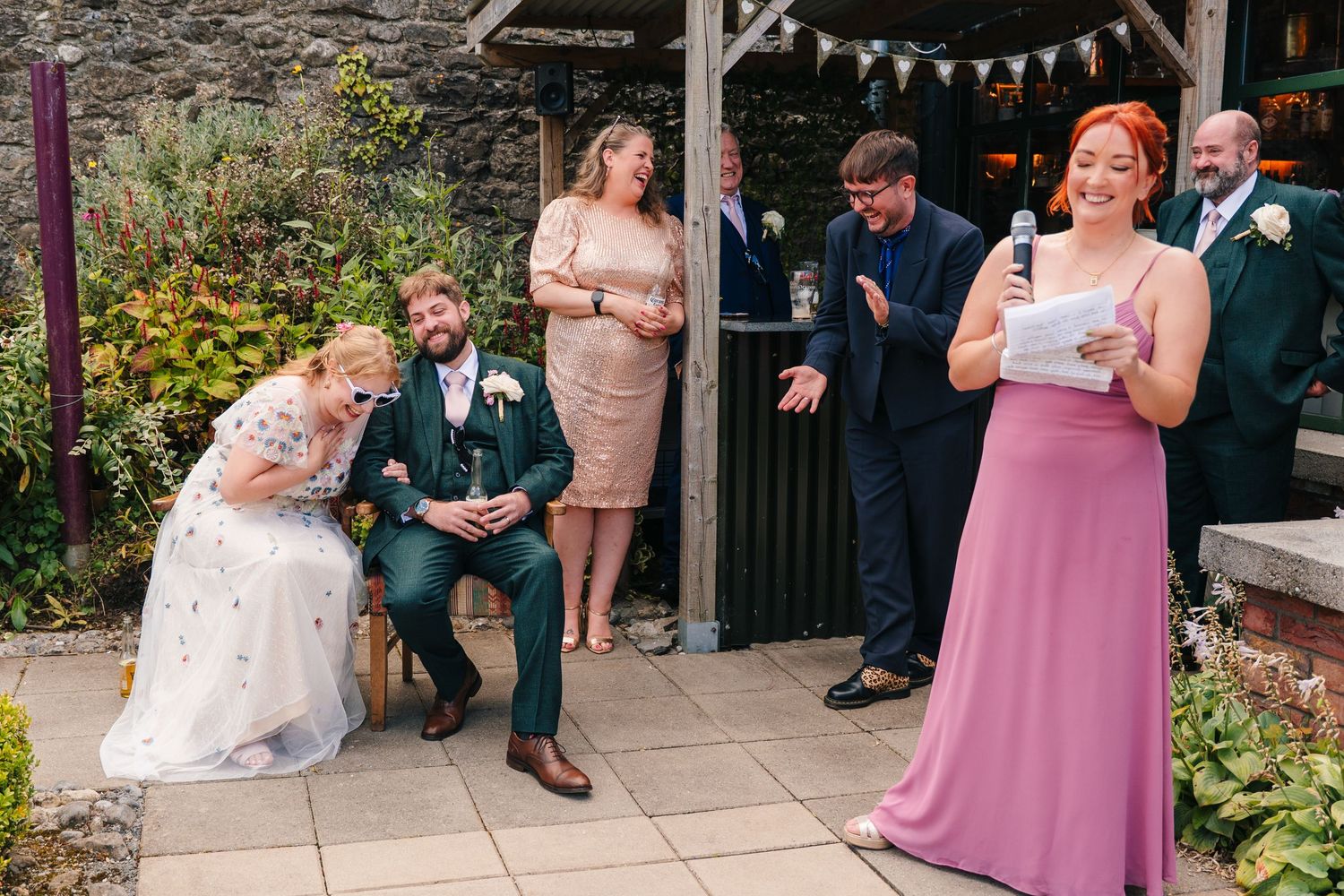 Wedding guests gather on a patio during an outdoor reception with bunting decoration. . Village Barn Tyrrellspass wedding photographer Irela