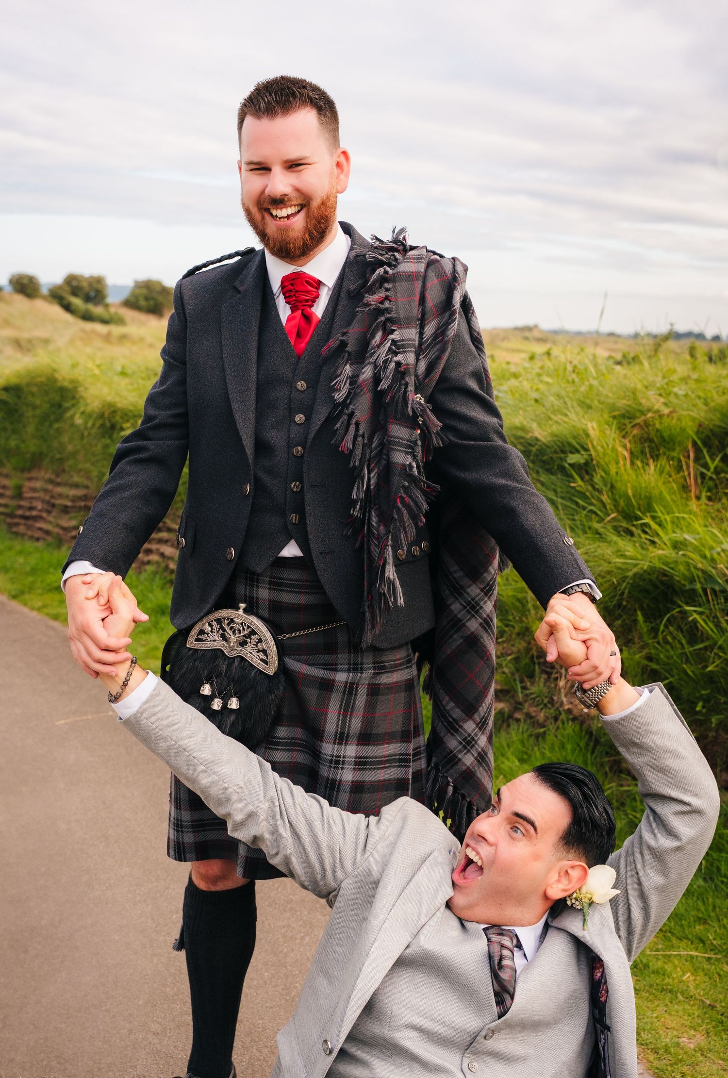 Two people sharing a playful moment on a pathway, with one wearing a kilt and formal Scottish attire. Portmarnock Hotel Wedding PHOTOGRAPHER