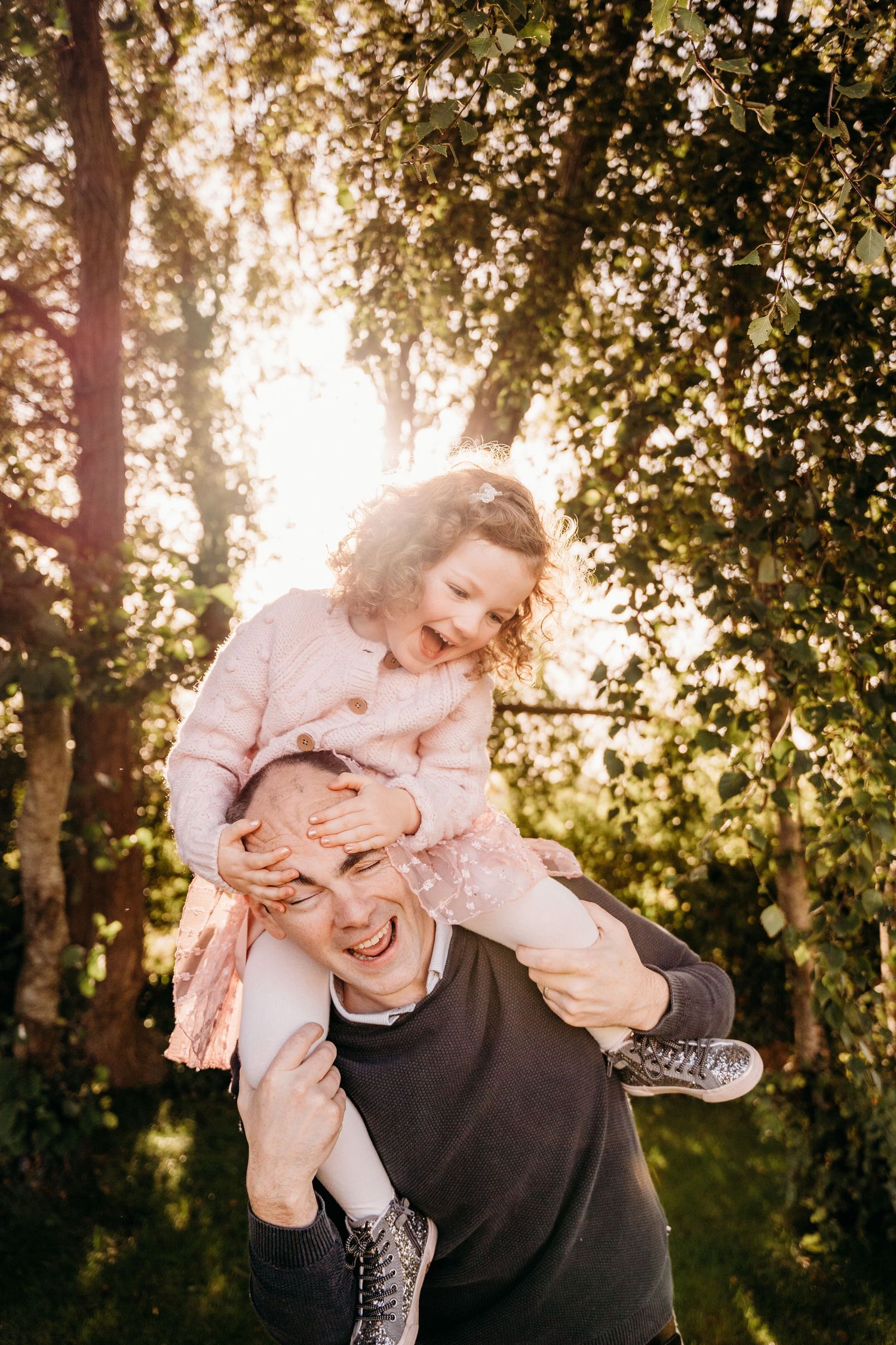 A playful parent and child sharing joyful moments outdoors during golden hour beneath sunlit trees. family PHOTOGRAPHER Dublin