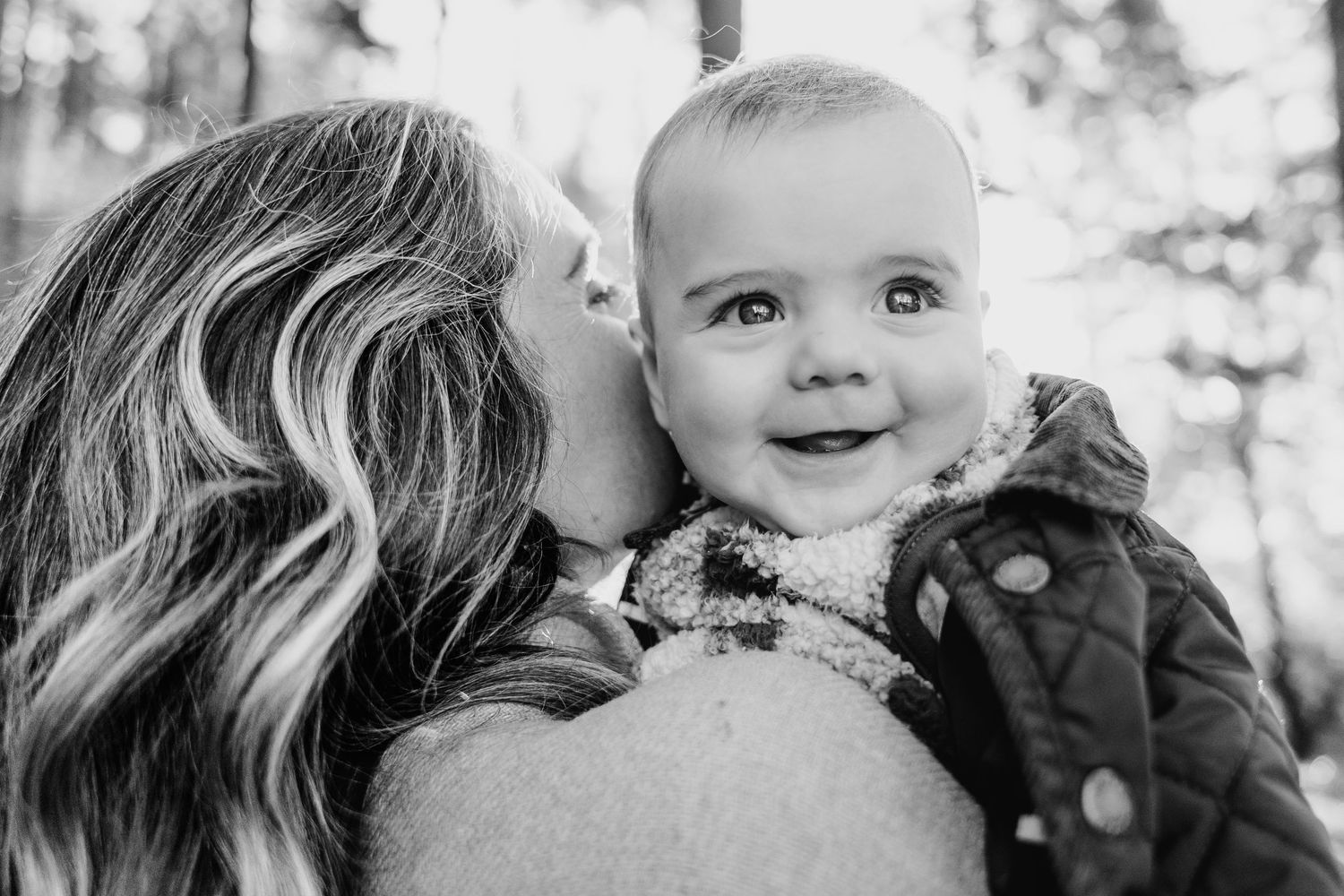 Black and white portrait of a smiling baby wearing a winter coat while being held outdoors. family PHOTOGRAPHER Dublin
