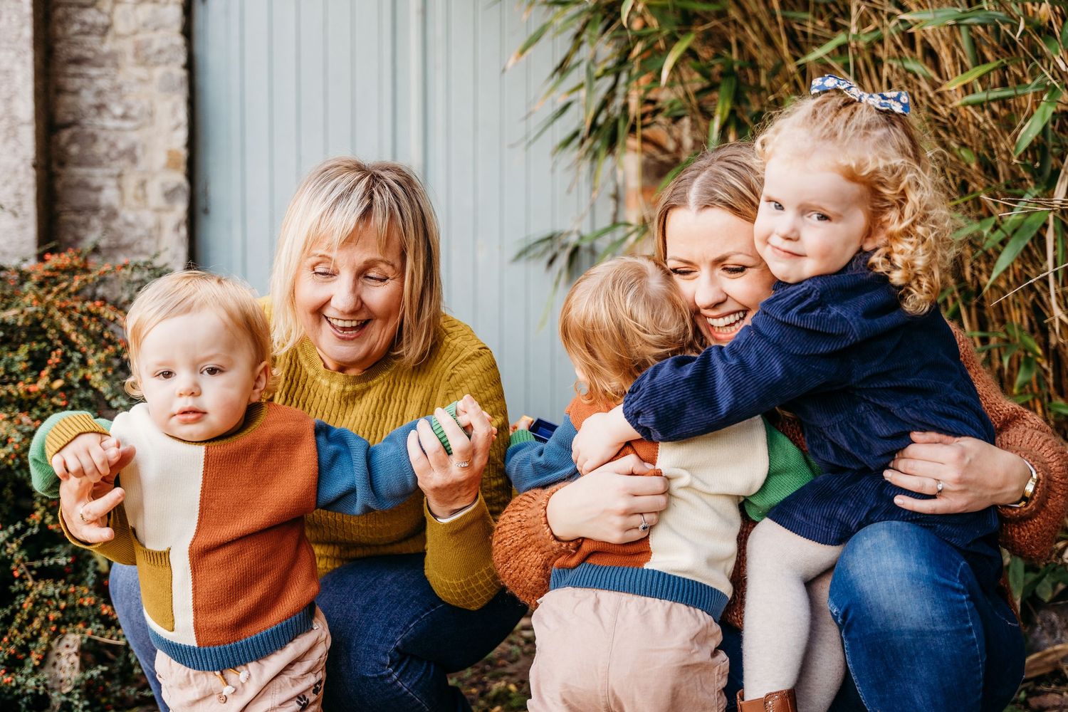 A cheerful group sits outside together near bamboo plants on a sunny autumn day, sharing smiles and warm embraces. family PHOTOGRAPHER Dubli
