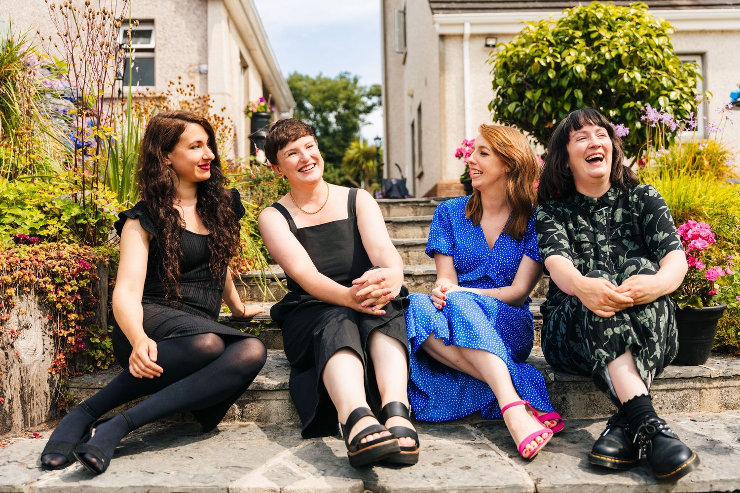 Four friends sit on outdoor steps laughing together while wearing contrasting black and blue outfits. Family PHOTOGRAPHER Dublin family PHOT