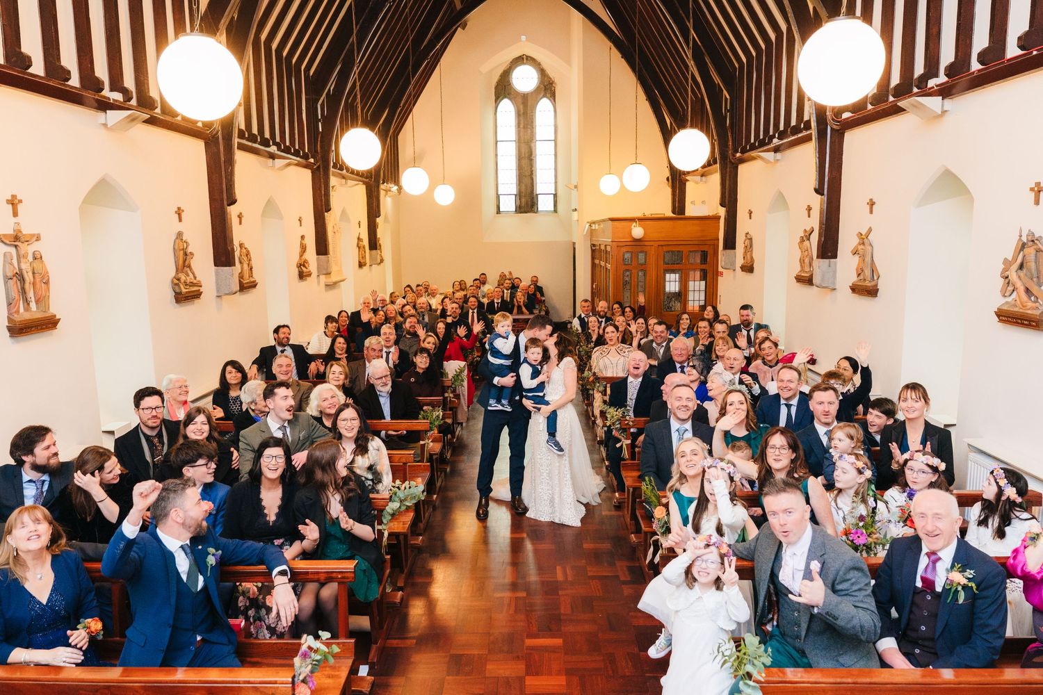 Interior of a traditional church with vaulted ceilings and glowing pendant lights during a ceremony.