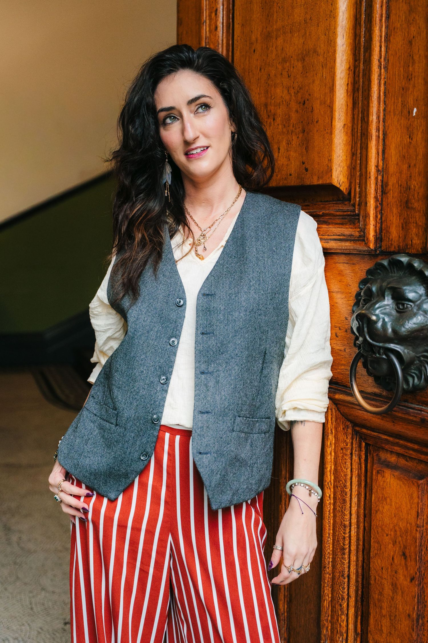 Fashion model wearing grey vest, white blouse and red striped pants against wooden door background. professional headshots dublin photograph