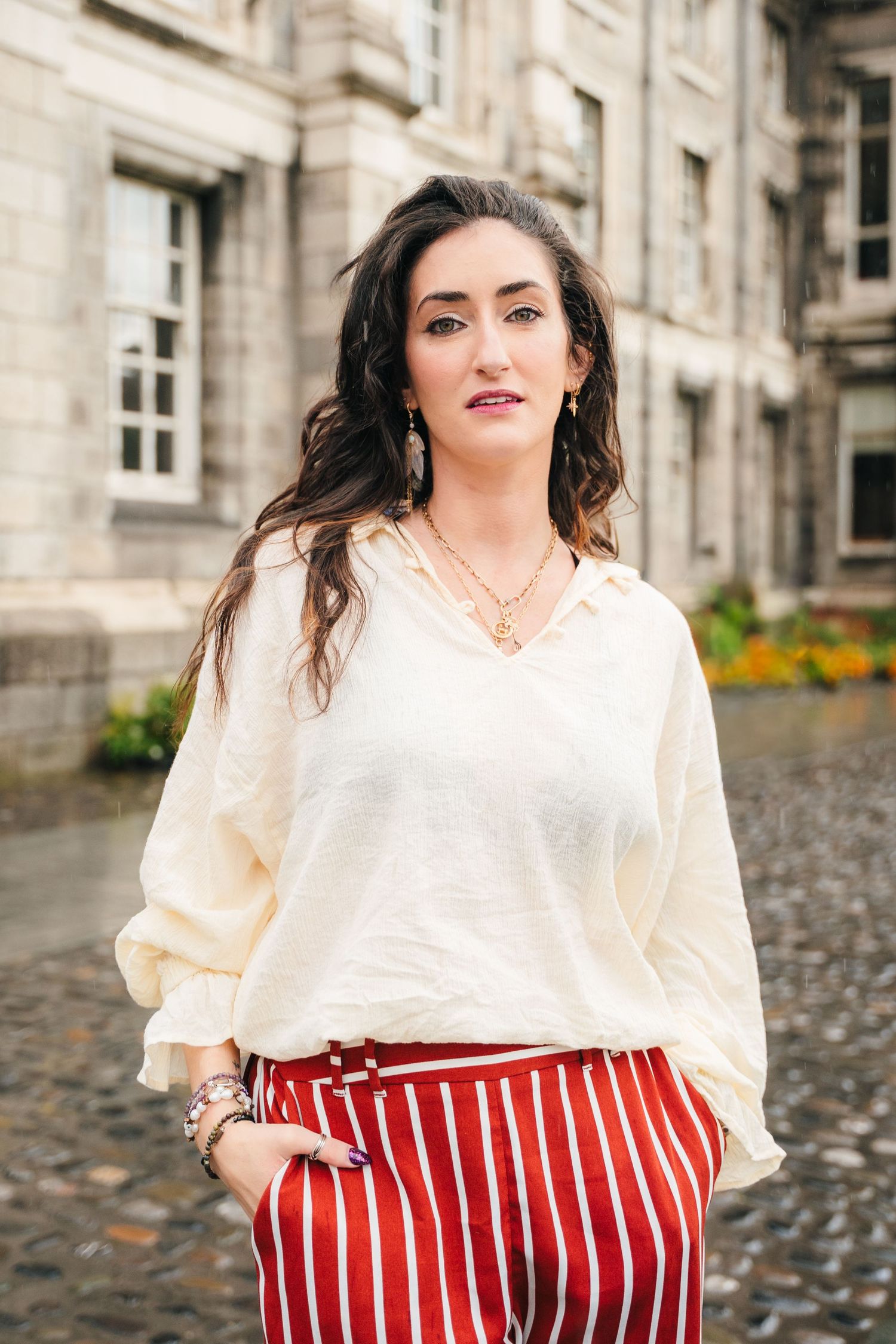 A fashion portrait featuring a cream colored blouse and red striped pants against a stone building backdrop. Headshots Dublin Photographer P