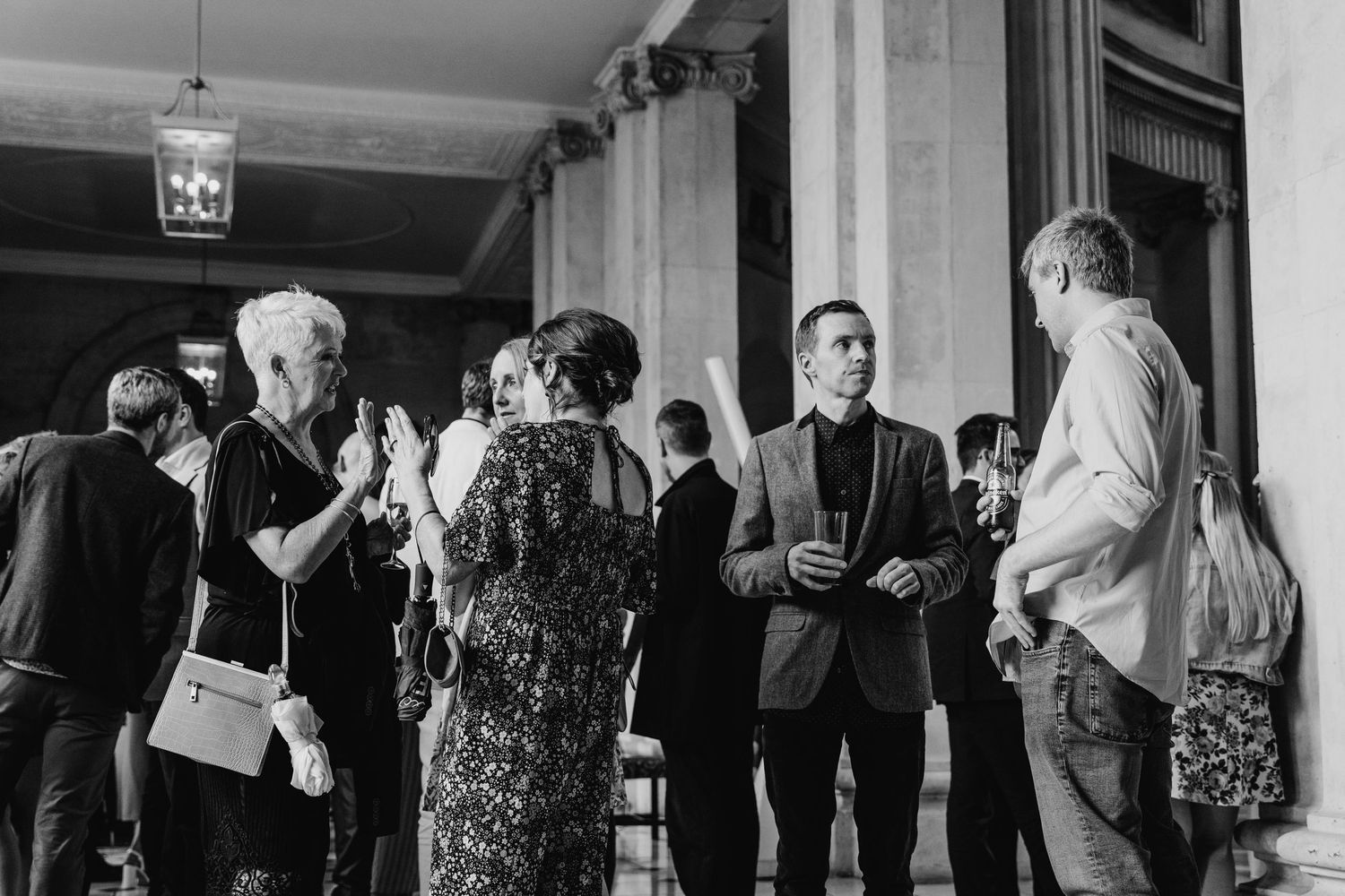 A black and white photo of people gathered in formal attire at a social event in an elegant hallway.  city hall dublin wedding photos