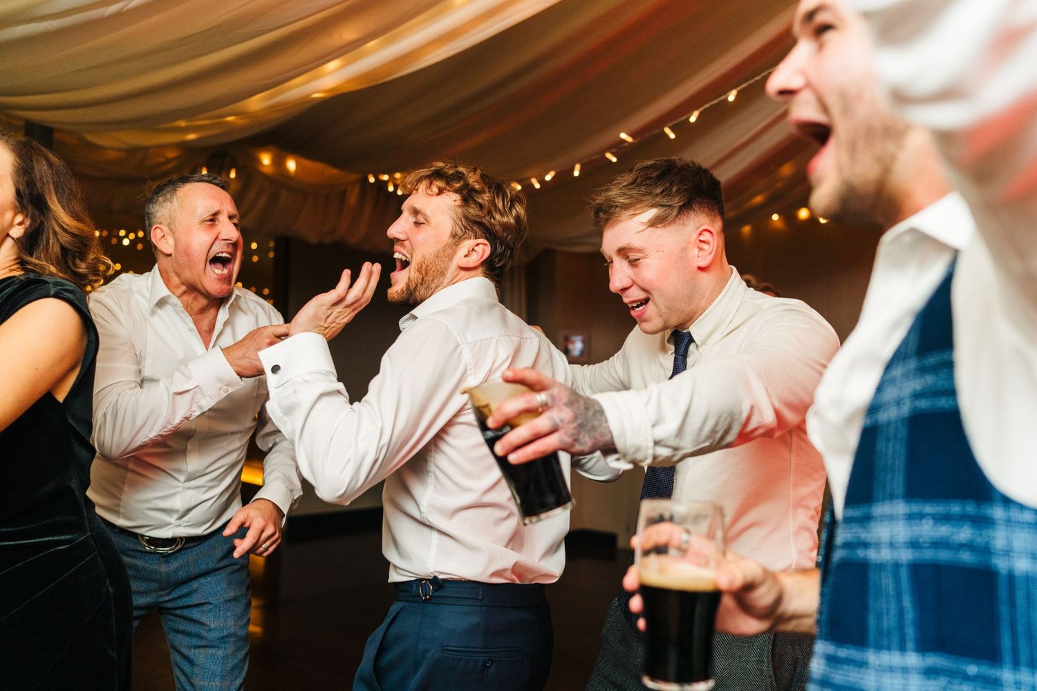 Wedding reception guests dancing and celebrating under draped fabric and string lights.  Virginia Park Lodge Wedding Photographer Cavan Dubl