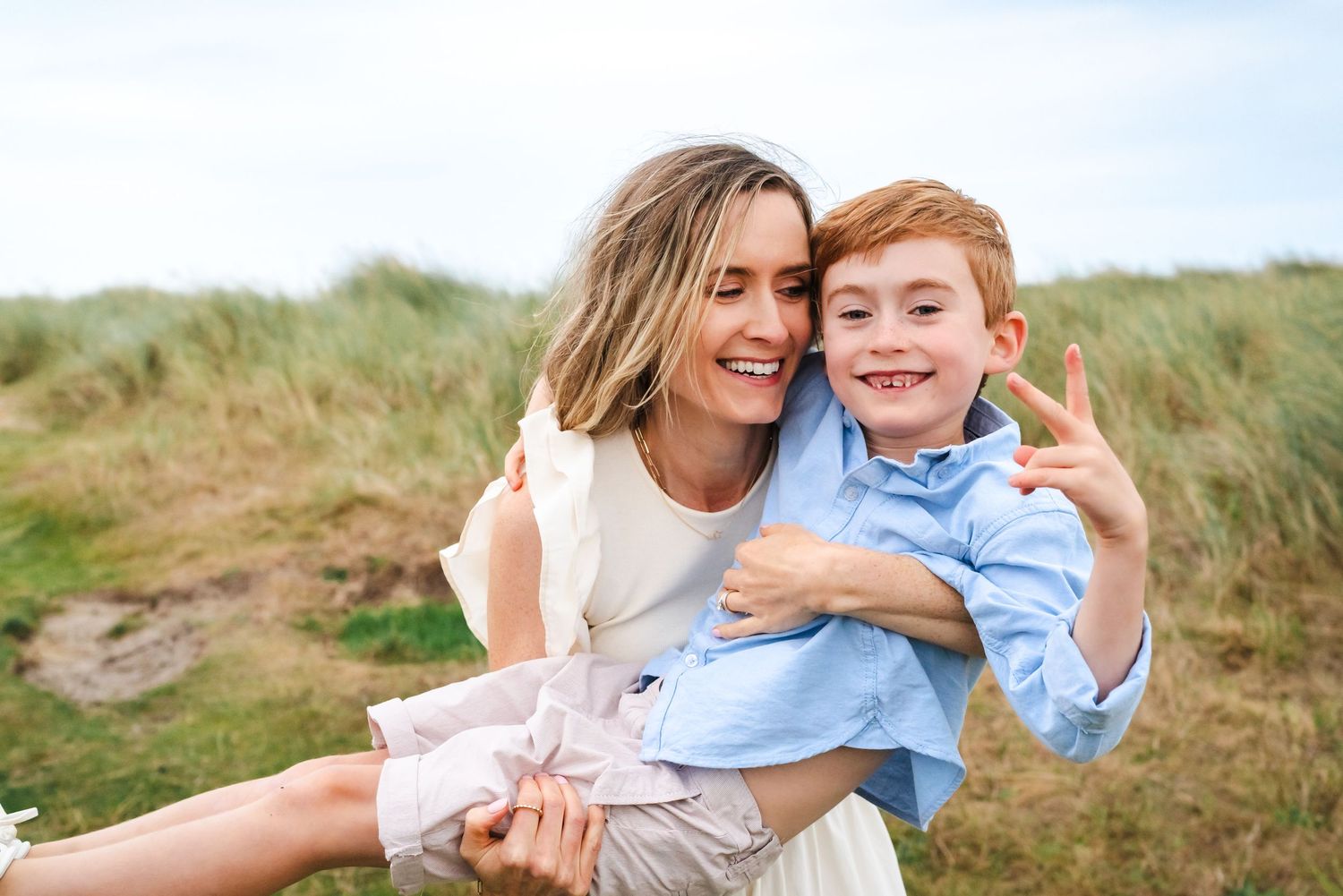 Tender family moments captured against coastal dunes and blue sky.  Family photographer Dublin Ireland