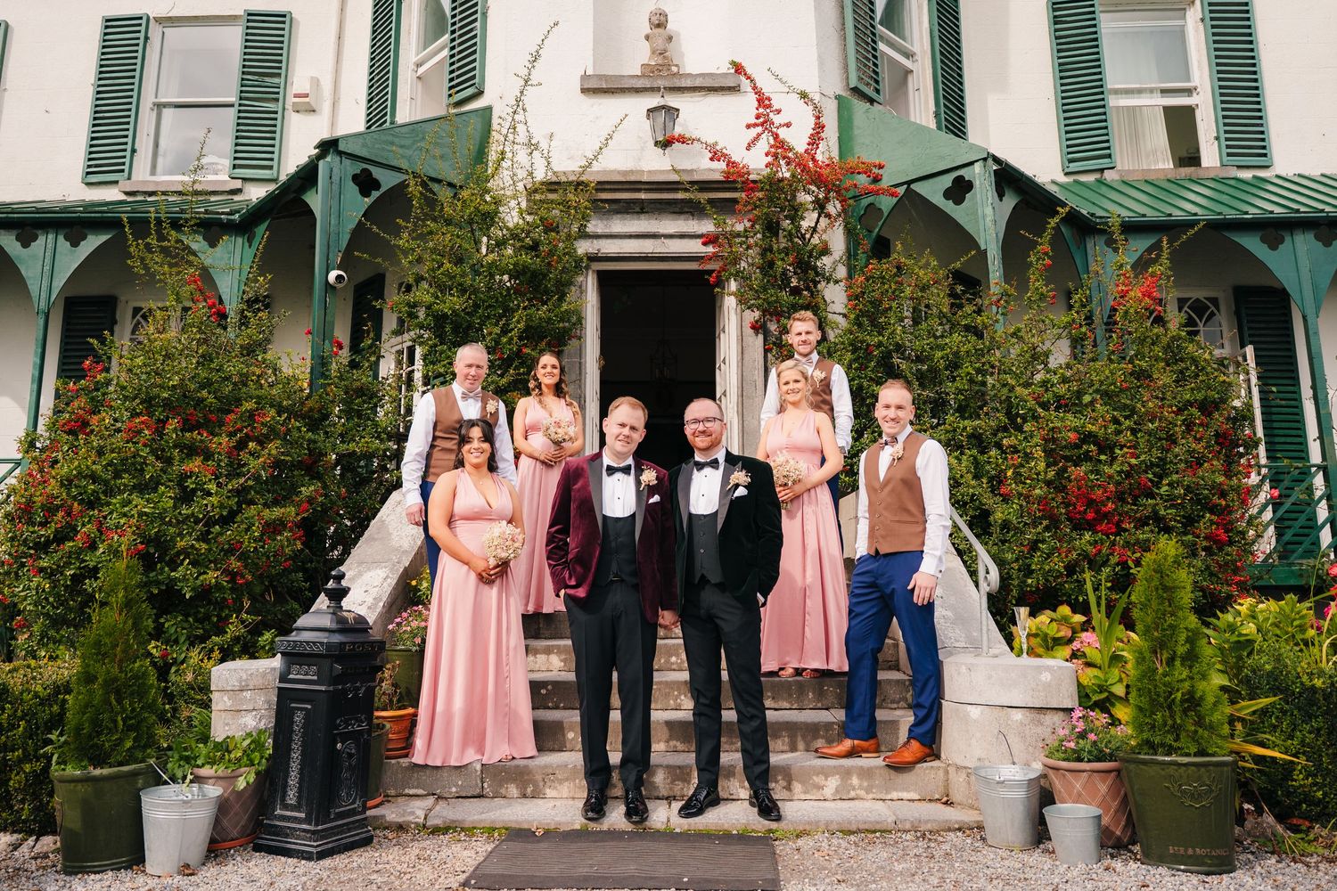 Wedding party in pink dresses and formal suits posing on steps of historic green house. LGBTQ Ashley Park Wedding Photographer