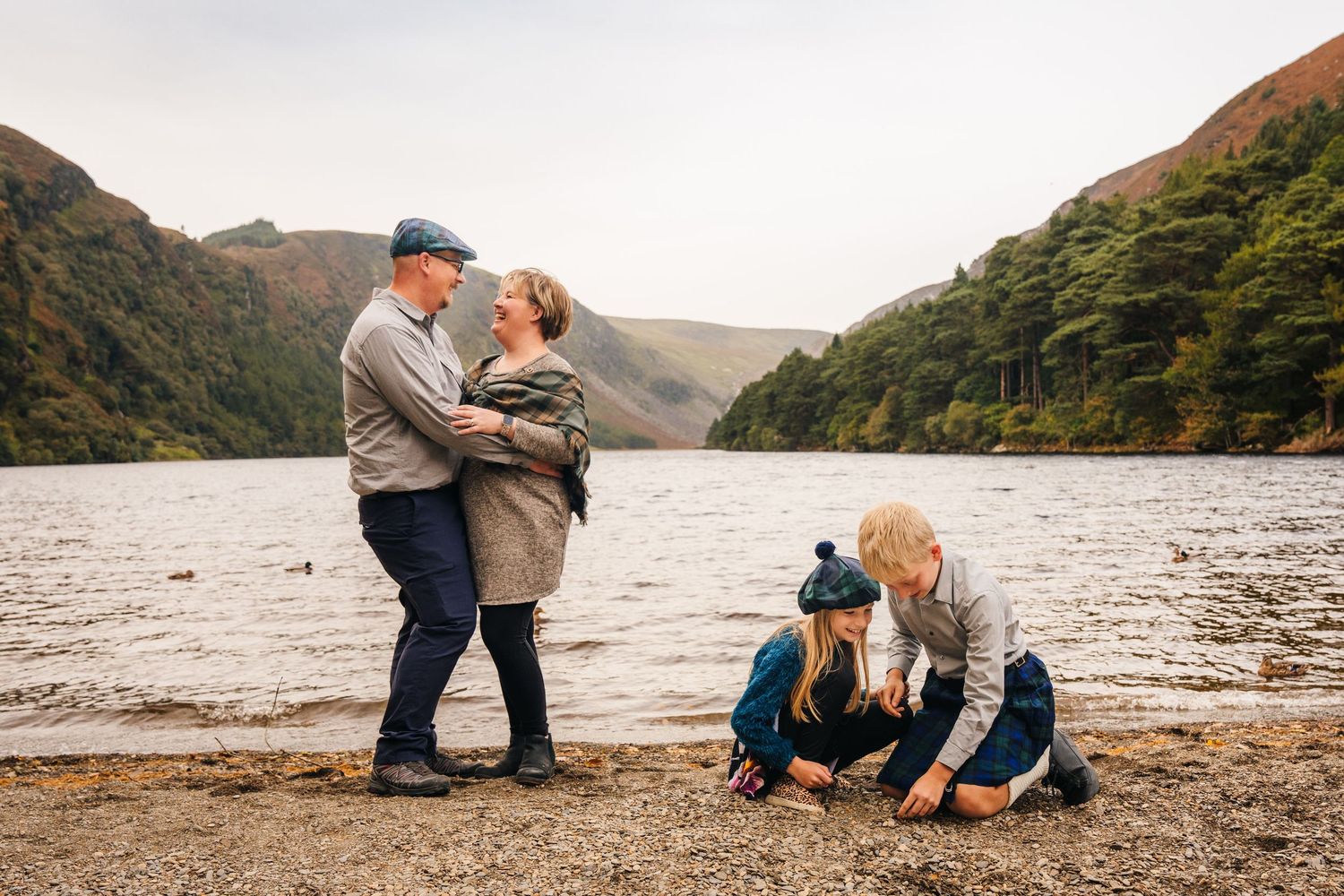 Candid family photo at a lakeside with mountains and forest in the background.Family photogrAPHER DUBLIN