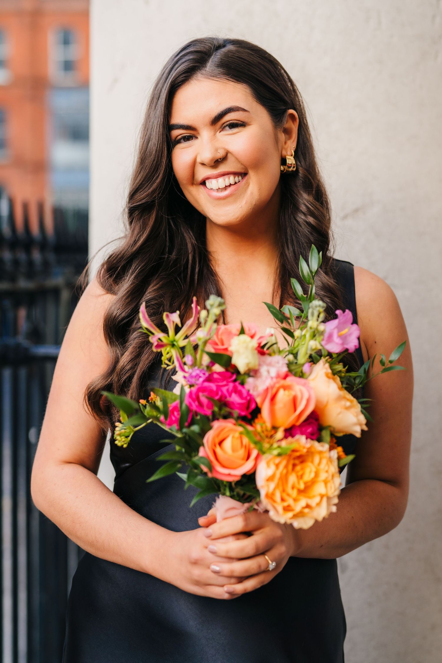 Bridesmaid in black dress holding vibrant bouquet of roses and flowers against urban backdrop. Wedding photographer dublin