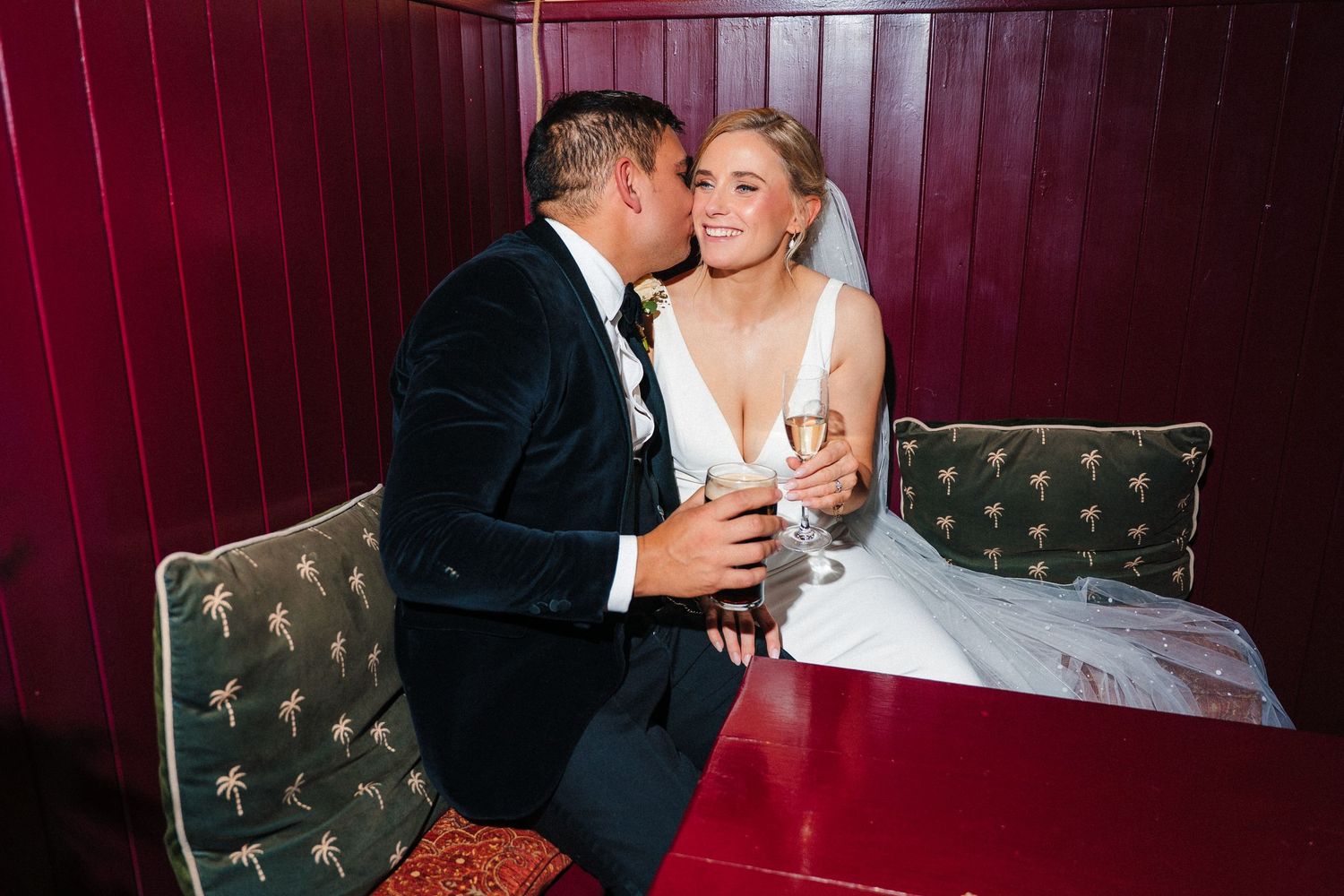 Couple shares intimate moment on red velvet seating at wedding reception. Ballymagarvey Wedding photographer