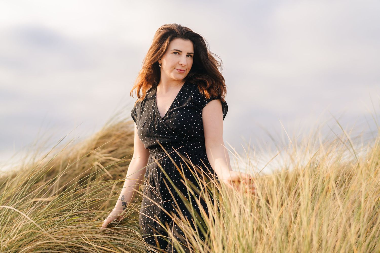 Person wearing dark polka dot dress sits gracefully among tall golden wheat fields at sunset. PHOTOGRAPHER Dublin ireland