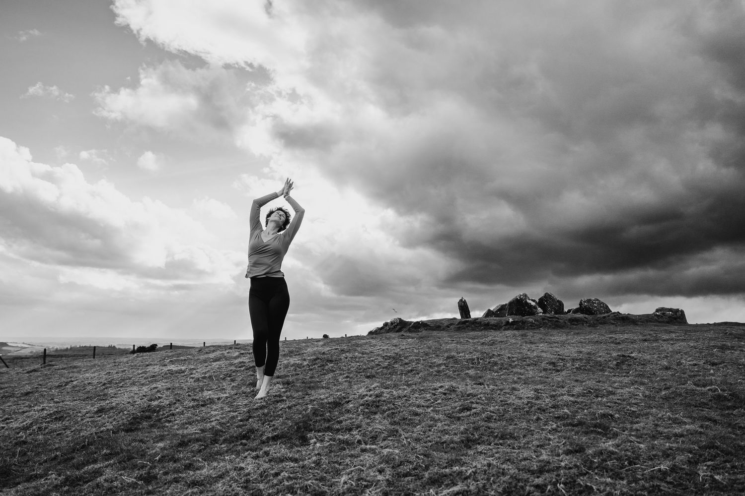 Silhouette of a figure with raised arms stands on a hilltop against dramatic cloudy skies in black and white. PHOTOGRAPHER Dublin ireland