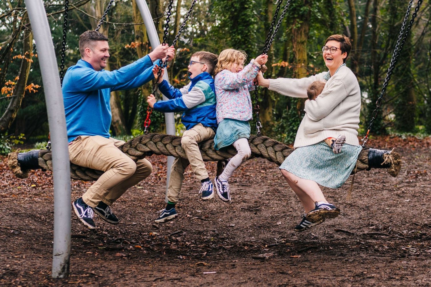 People enjoy a playful moment on a park swingset together in a wooded outdoor setting. family PHOTOGRAPHER Dublin