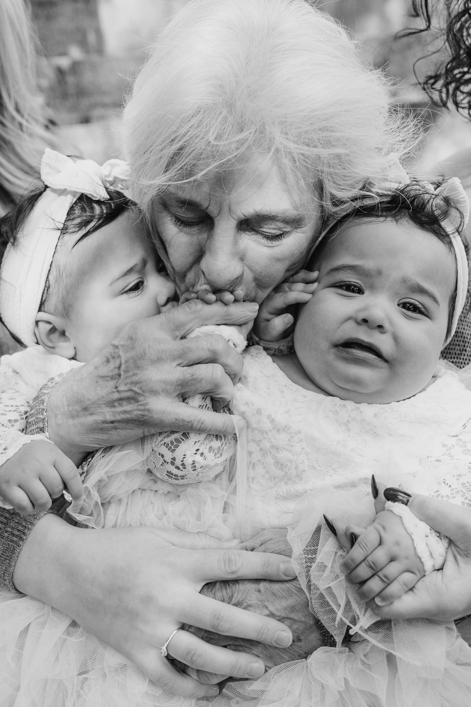 A tender black and white portrait of a grandmother embracing two babies in white dresses. family PHOTOGRAPHER Dublin