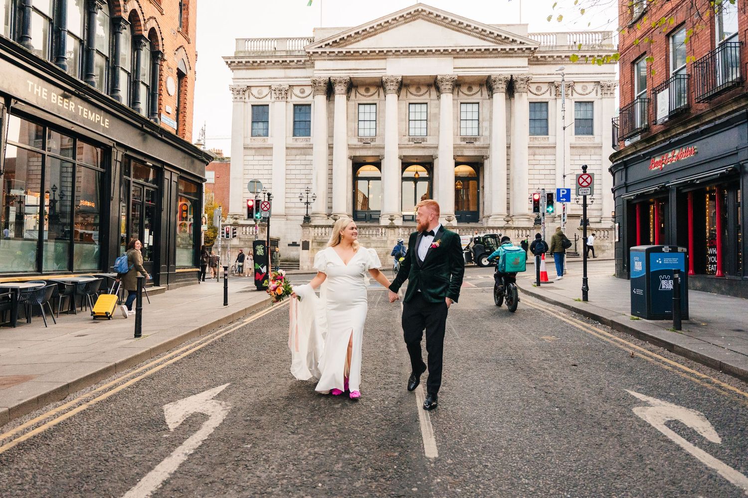 Newlyweds running down a city street with a grand neoclassical building in the background. City Hall Dublin Photographer