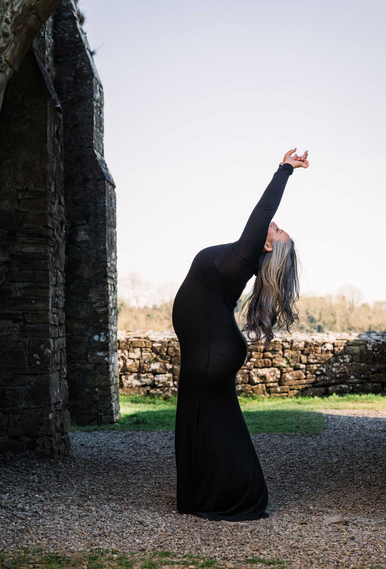 Graceful silhouette in long black dress poses against stone ruins at sunset. Family PHOTOGRAPHER Dublin